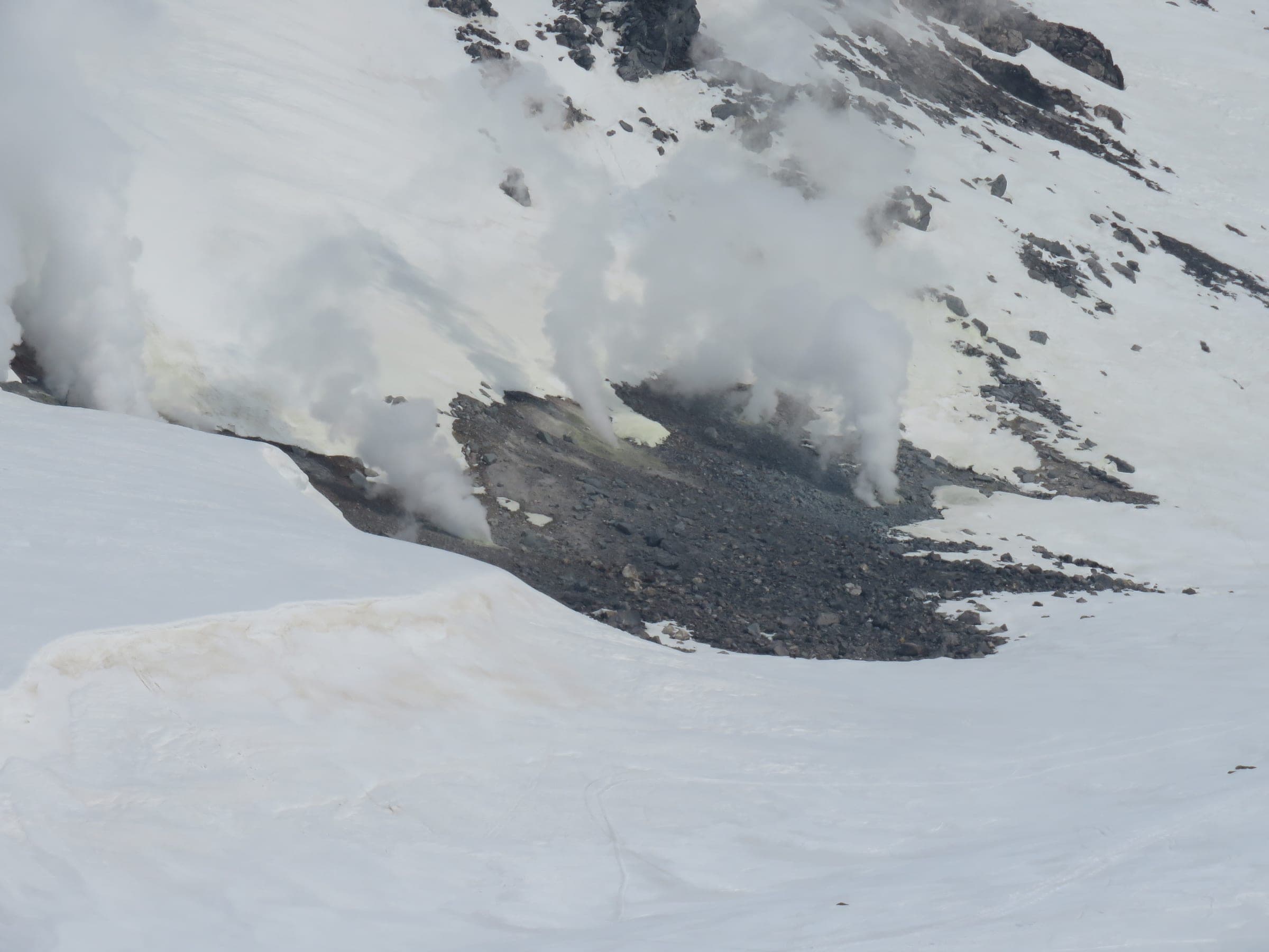 Steam rises from dark volcanic vents in the snow on the slopes of Asahidake