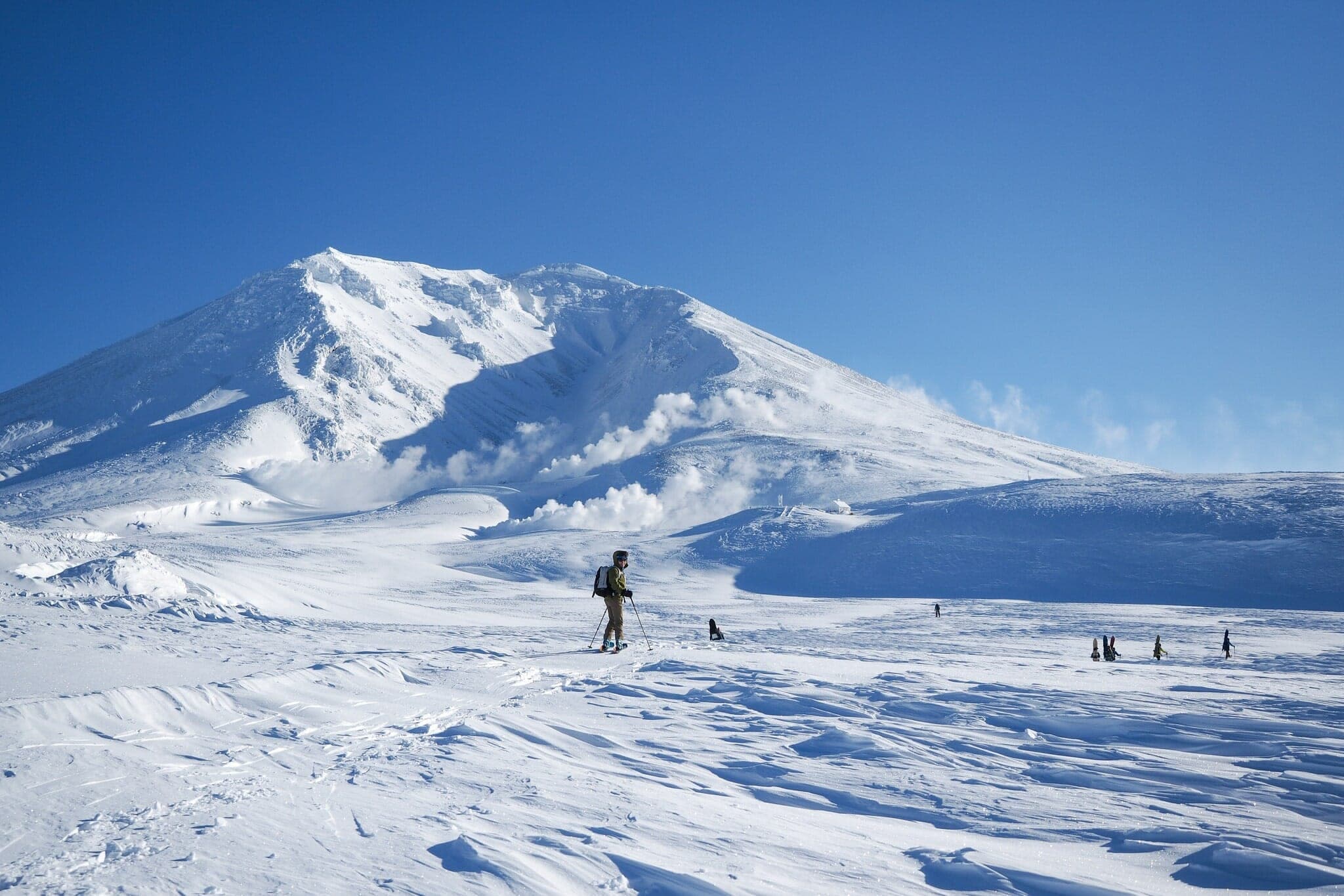 A lone ski tourer heads across open snow toward the white summit cone of Asahidake