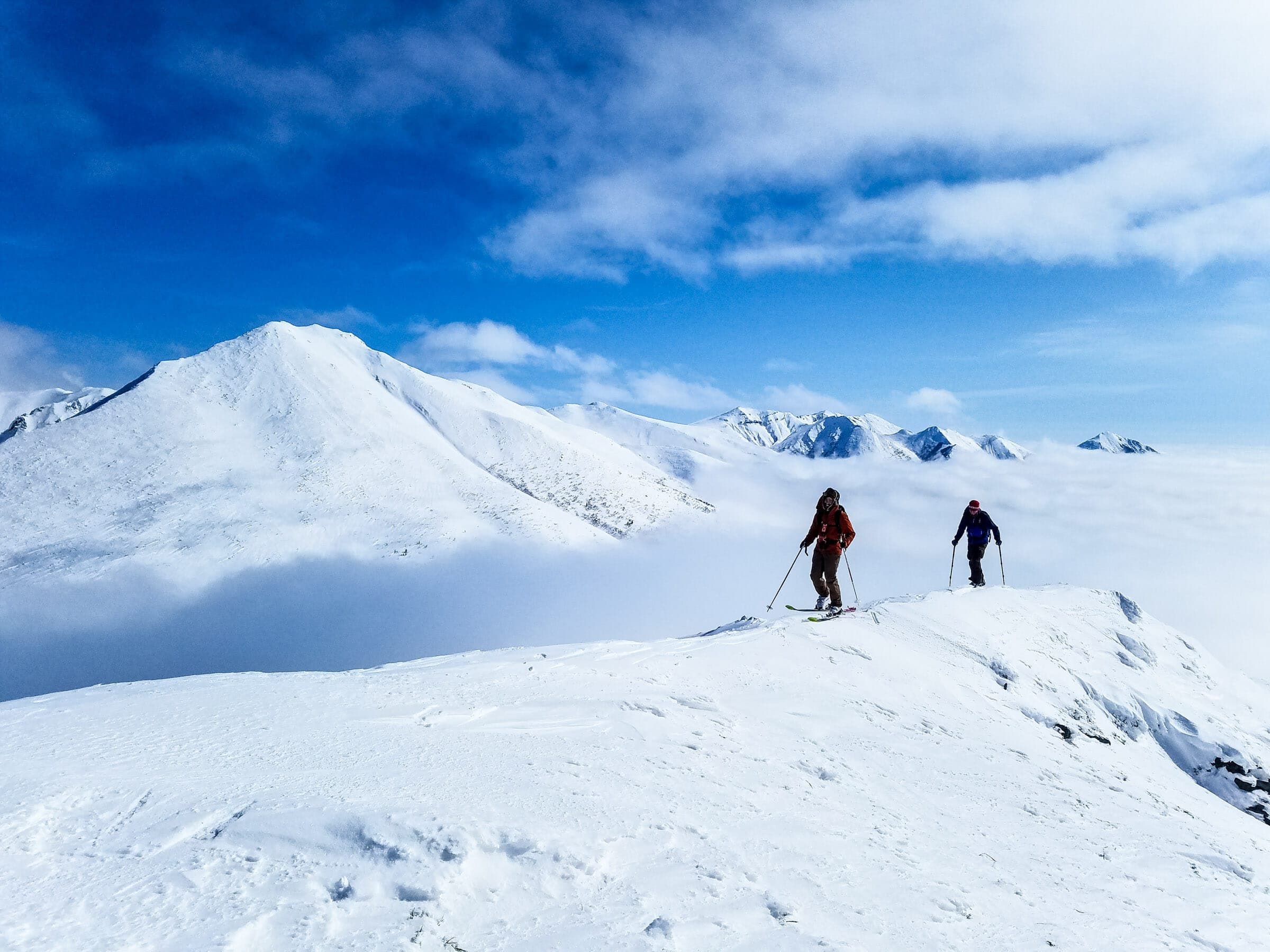 Two ski tourers climb a snowy ridge toward the summit of Maefurano-dake