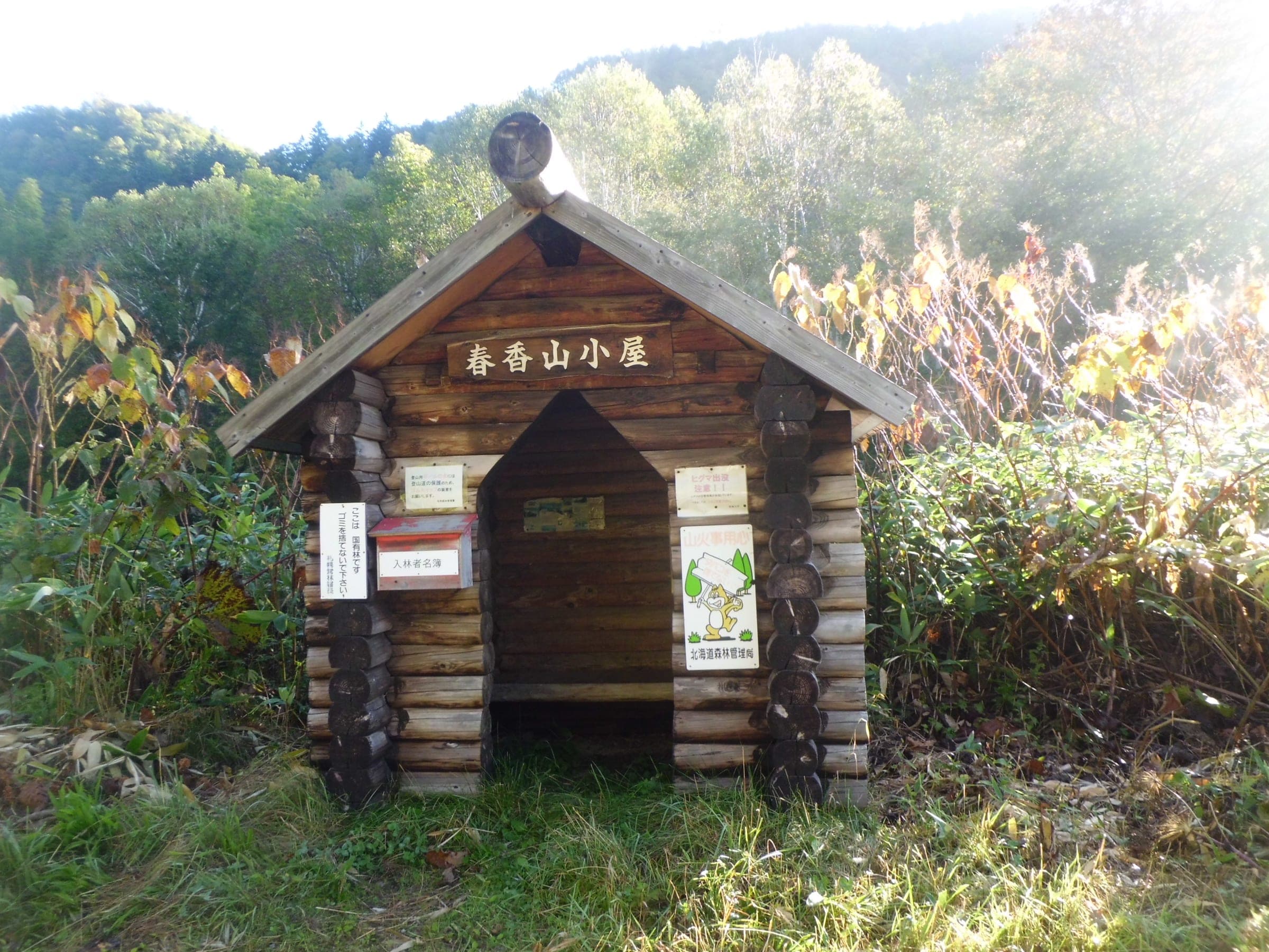 A small log shelter called Harukayama Hut sits in autumn scrub on Haruka-yama