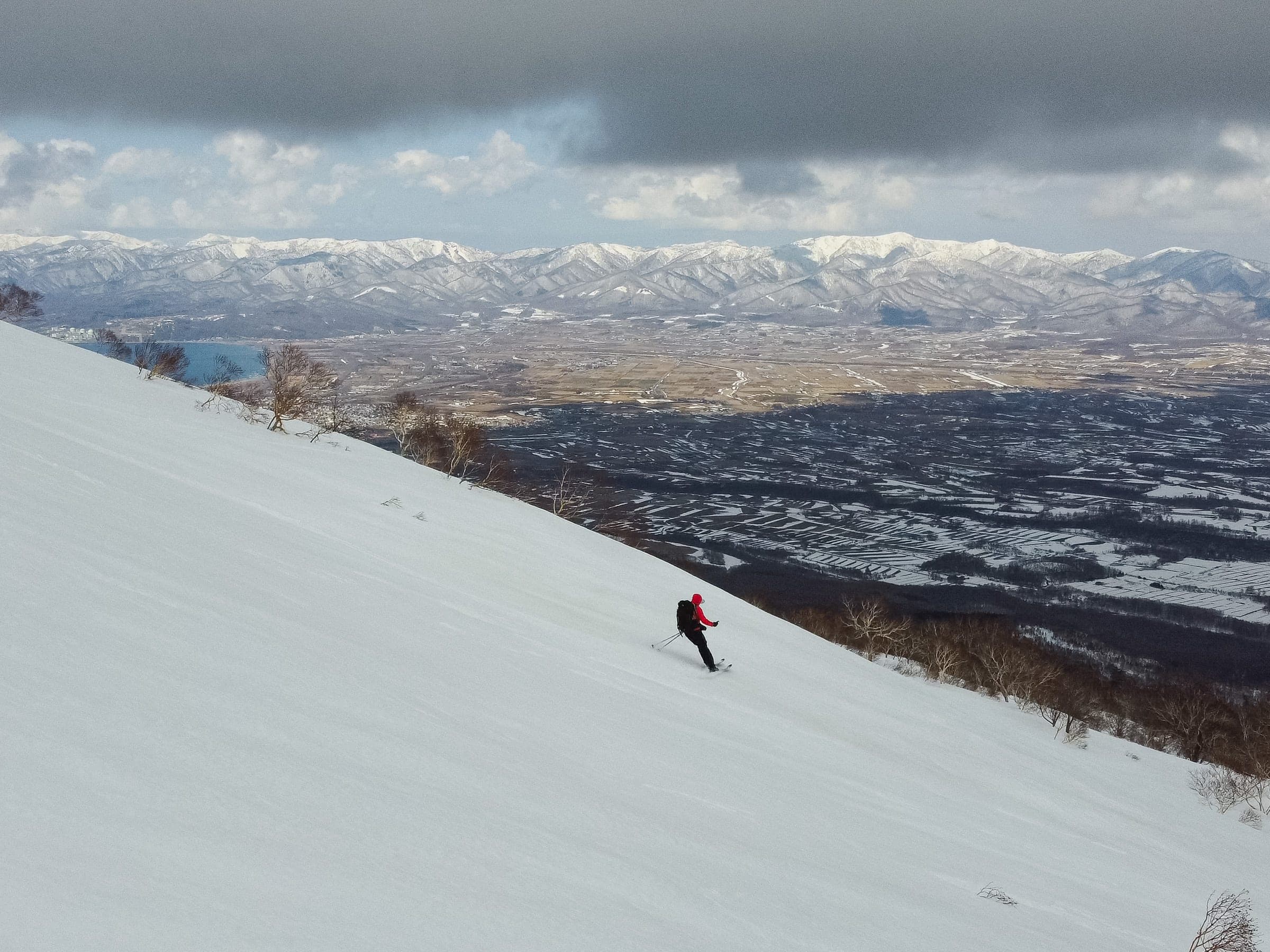 A skier descends a long open slope on Iwanai-dake above Iwanai town and the sea