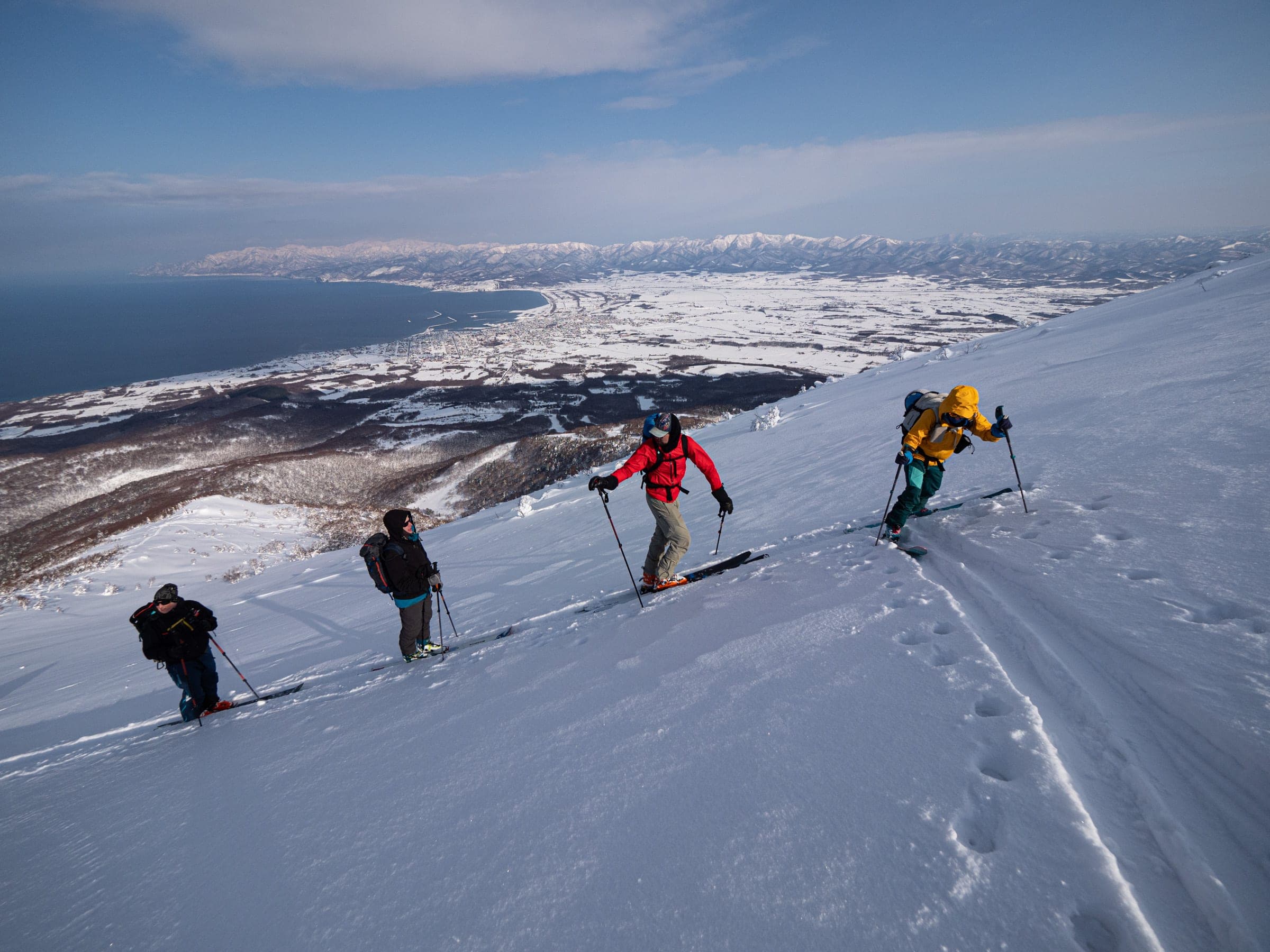 A line of ski tourers climbs above the Sea of Japan coast on Iwanai-dake
