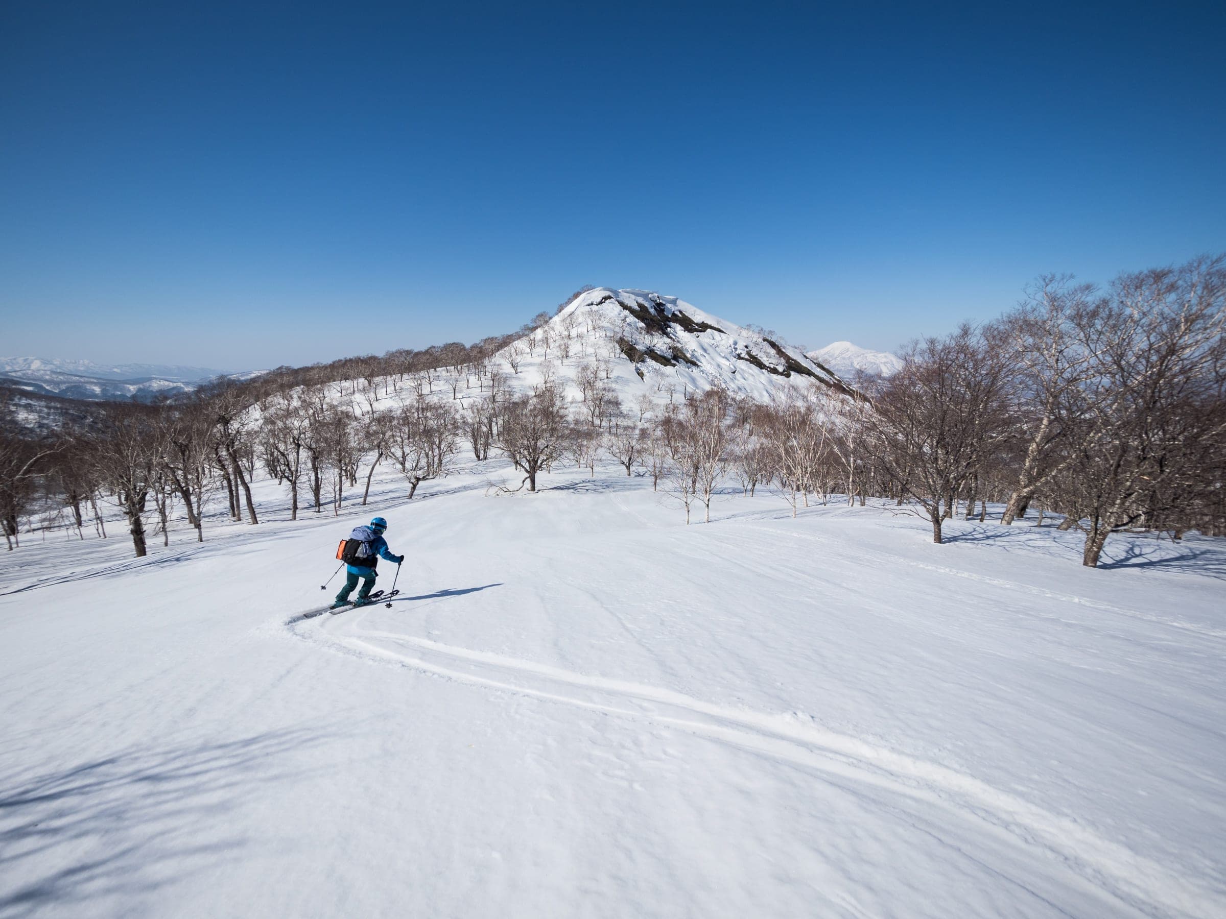 A skier crosses an open slope below the pointed summit of Konbu-dake