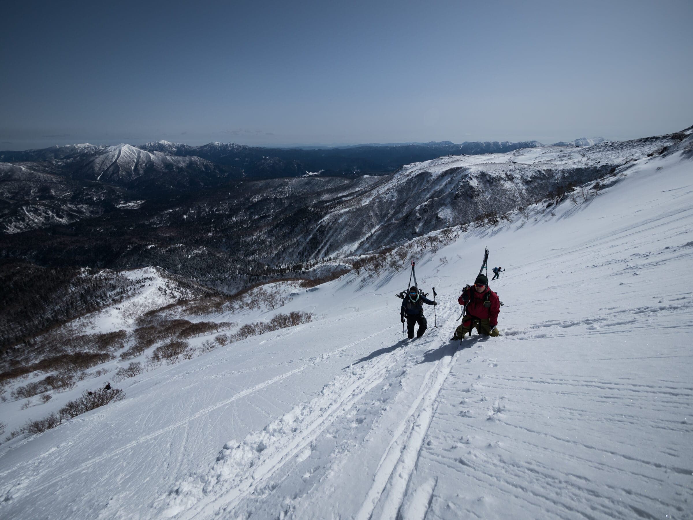 Two skiers rest on a snowy shoulder of Kurodake with the Daisetsuzan peaks behind