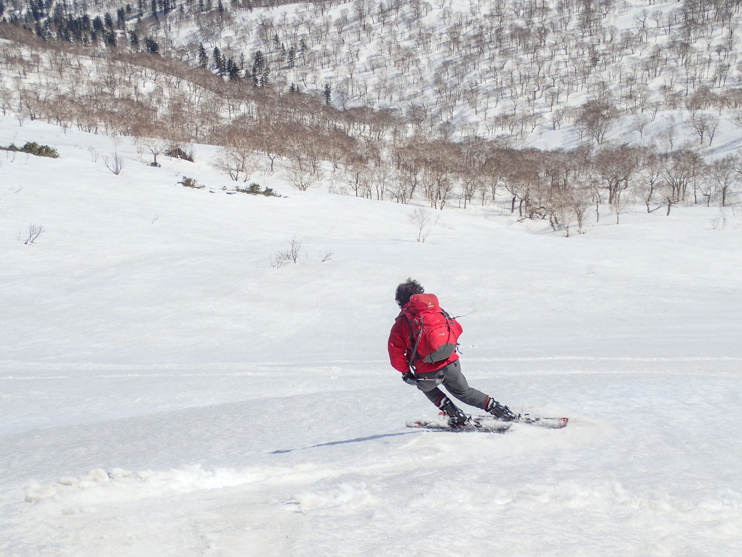 A skier in red carves across open snow on the traverse from Muine-yama