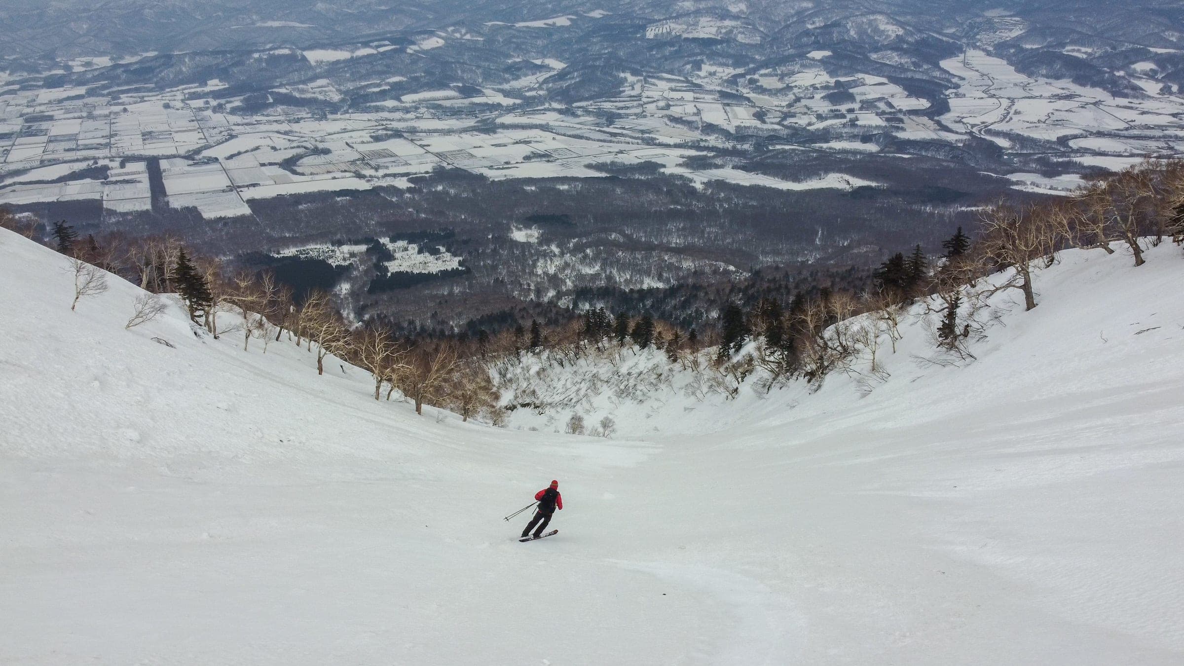 A skier rides down the long 148 Gully on Mt. Yotei with farmland far below