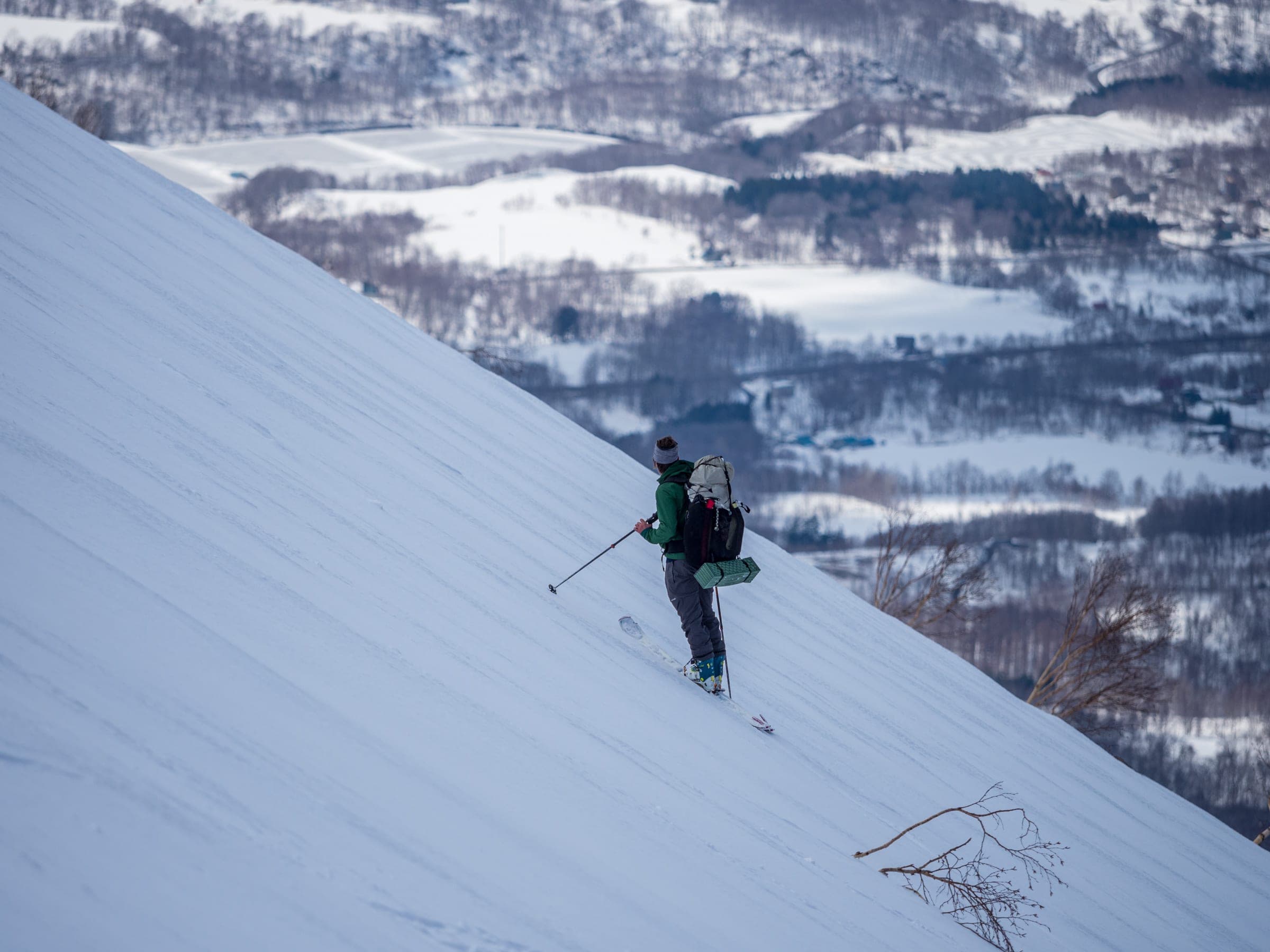 A ski tourer climbs a steep upper slope of Mt. Yotei's Hirafu route above the farmland