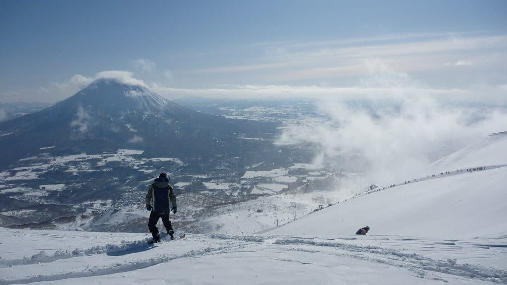 A snowboarder drops toward the clouds on the Niseko range with Mt. Yotei across the valley