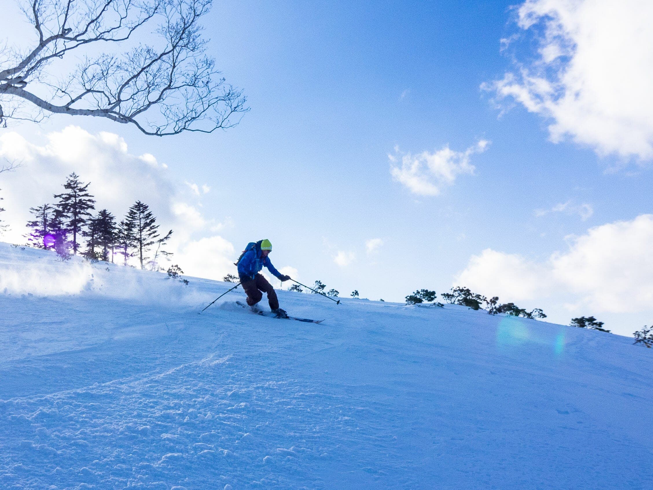 A skier turns down the open north ridge of Nissho Peak under blue sky