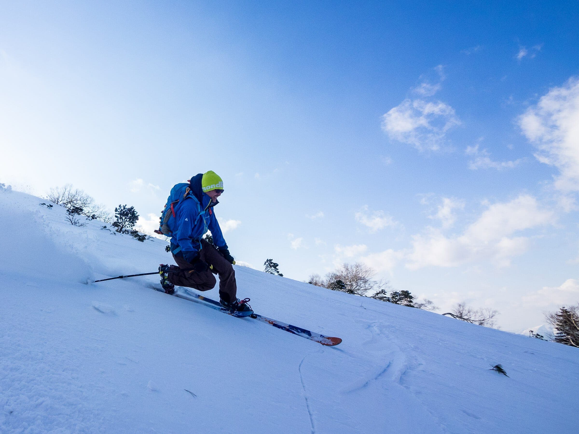 A skier in blue descends a bright slope on Nissho Peak under scattered cloud