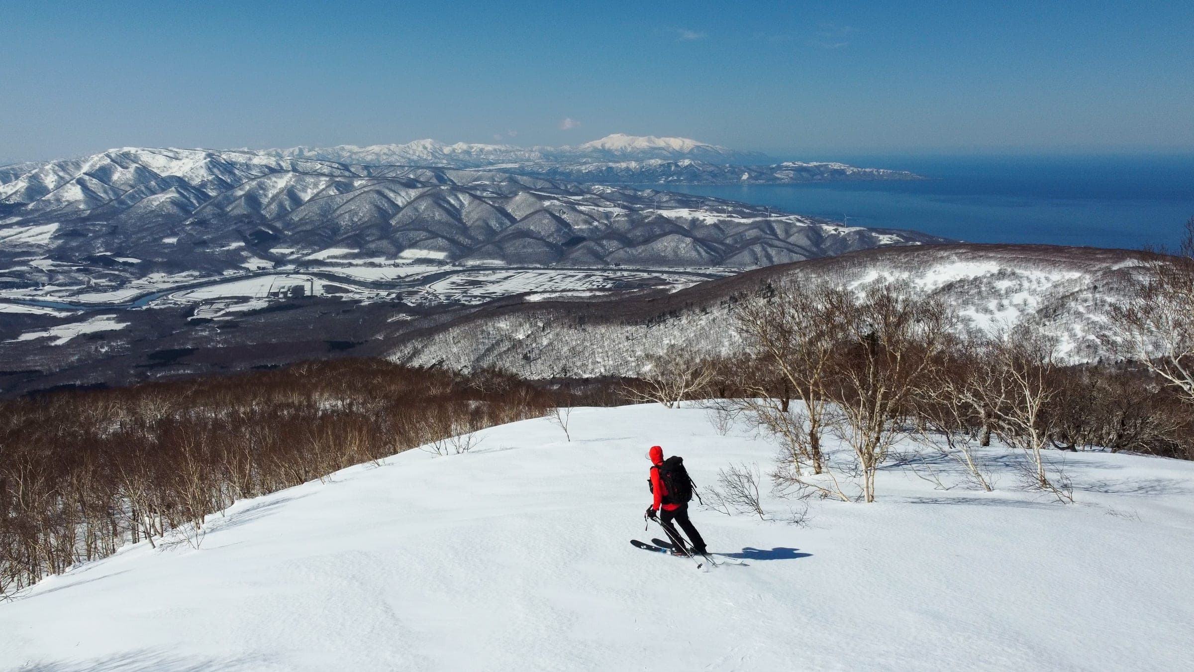 A skier descends broad slopes on Raiden-yama with the Sea of Japan below