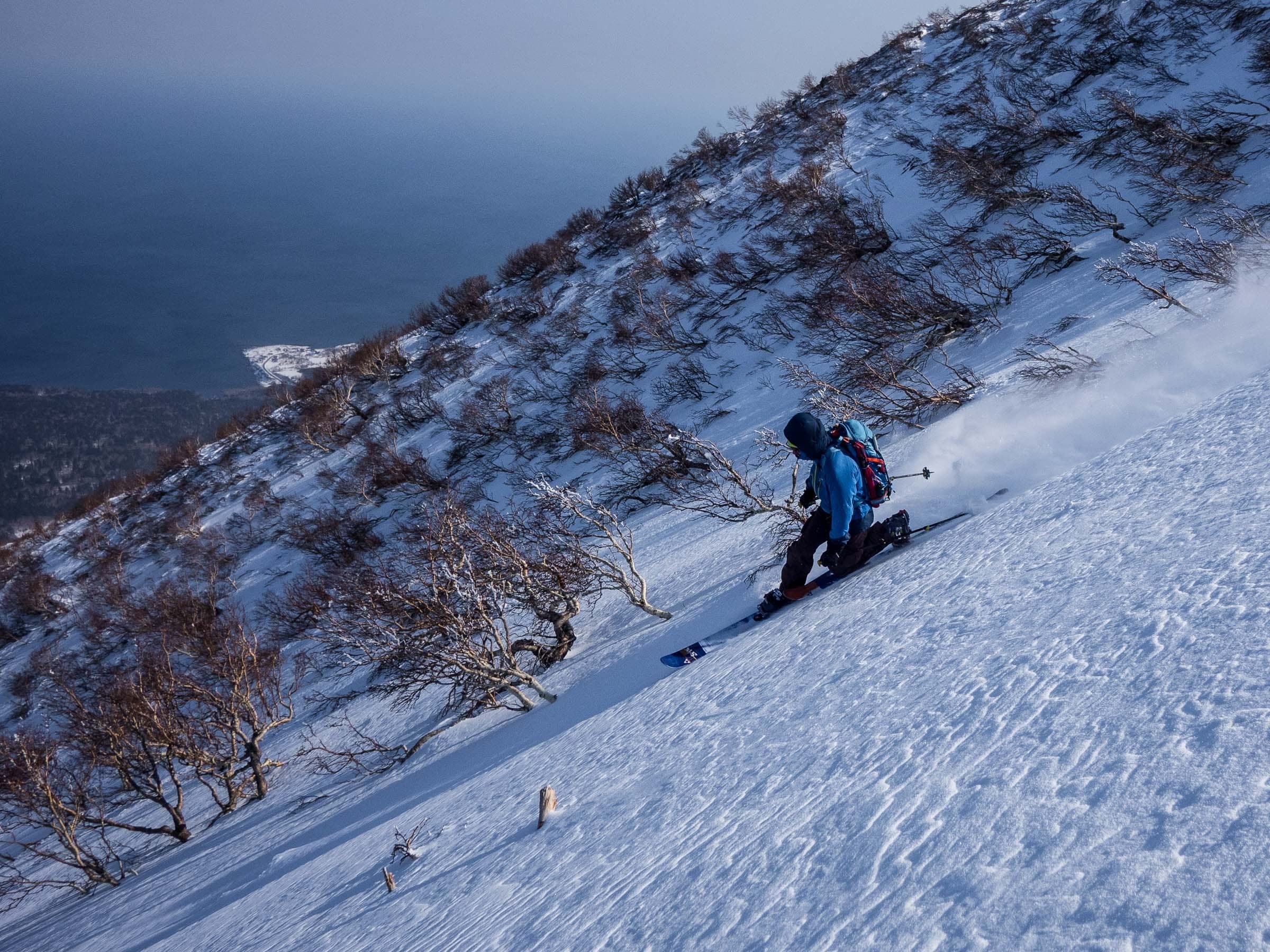 A snowboarder carves a steep slope on Rishiri-zan's Oshidomari ridge above the sea