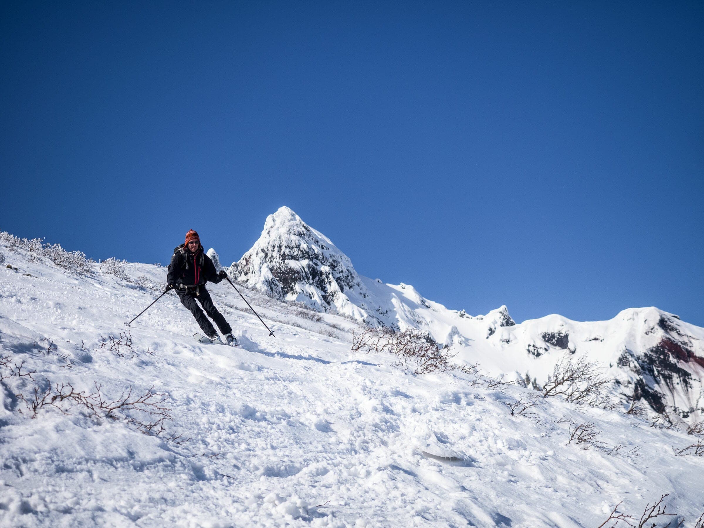 A skier turns below the jagged summit spire of Rishiri-zan under a deep blue sky
