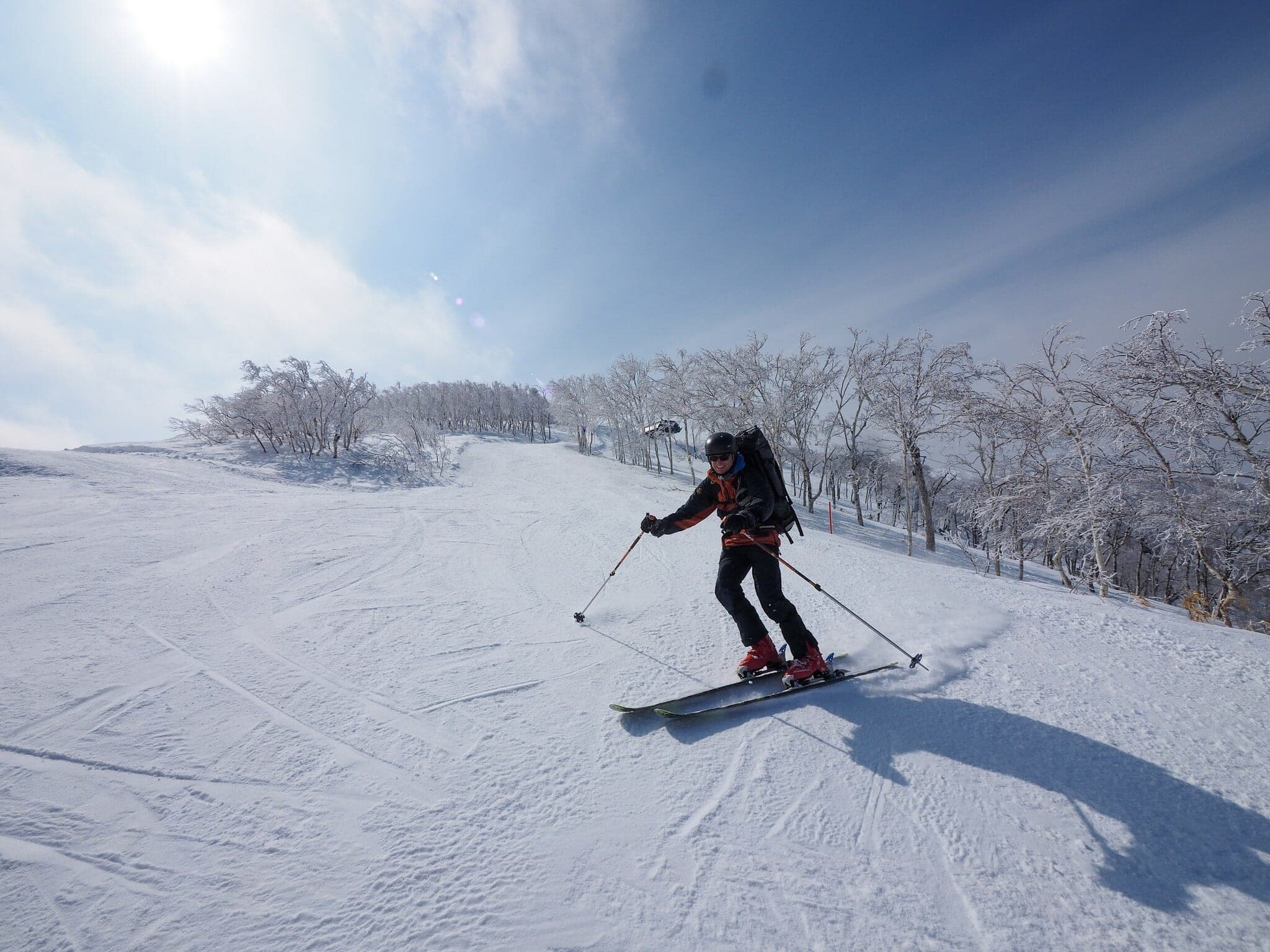 A ski tourer glides down a sunny slope on Sahoro-dake through rimed trees