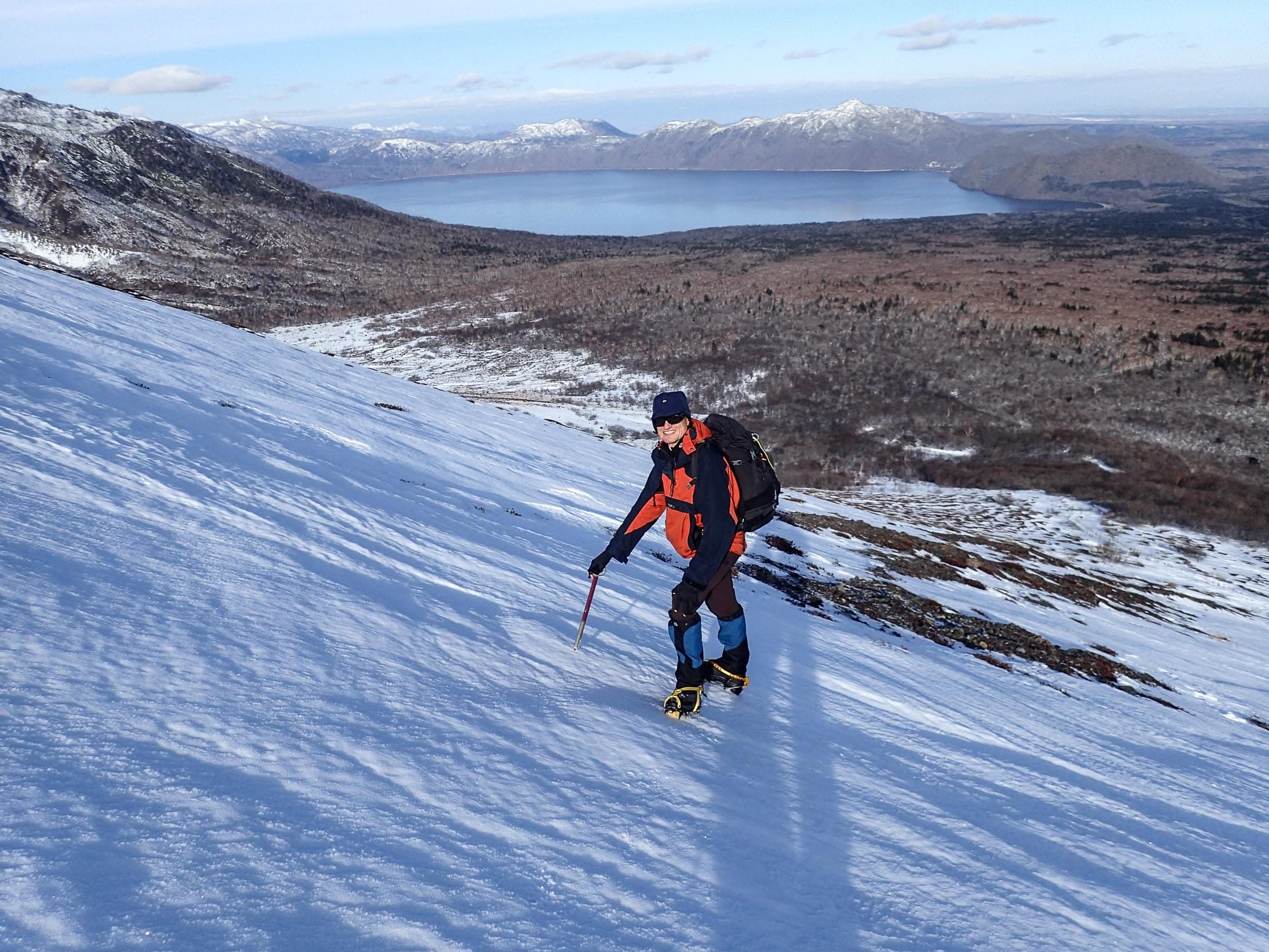 A ski tourer in crampons climbs the outer rim of Tarumae-zan with Lake Shikotsu below