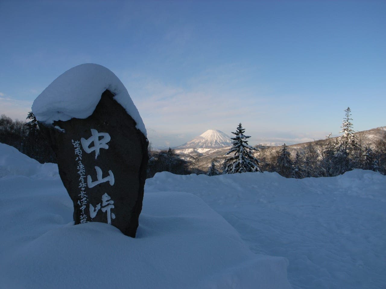 The Nakayama Pass stone under deep snow at Michi-no-eki Boyo Nakayama, with Mount Yotei behind