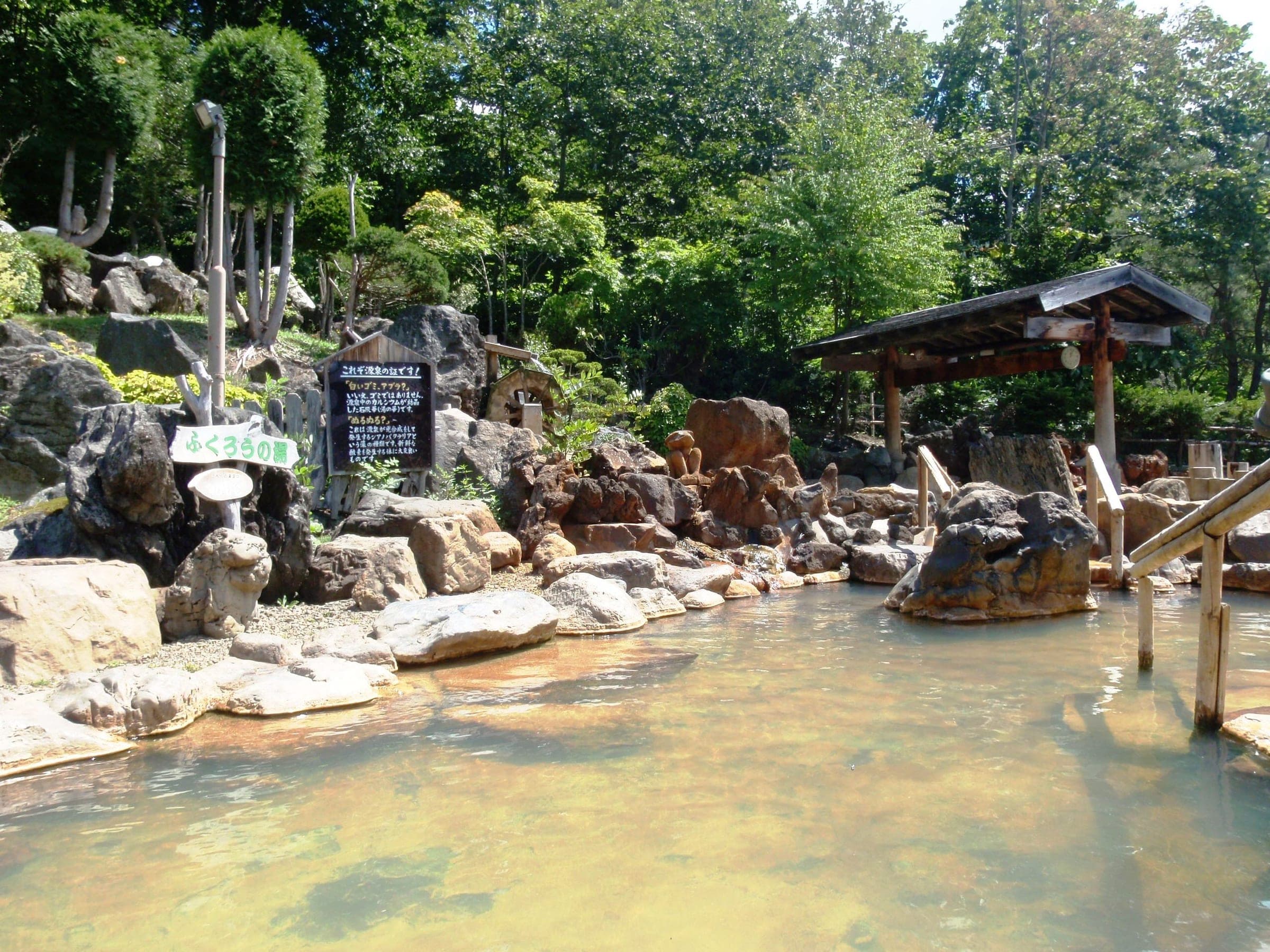 Rocks and a wooden shelter surround the large outdoor bath at Hoheikyo Onsen in summer