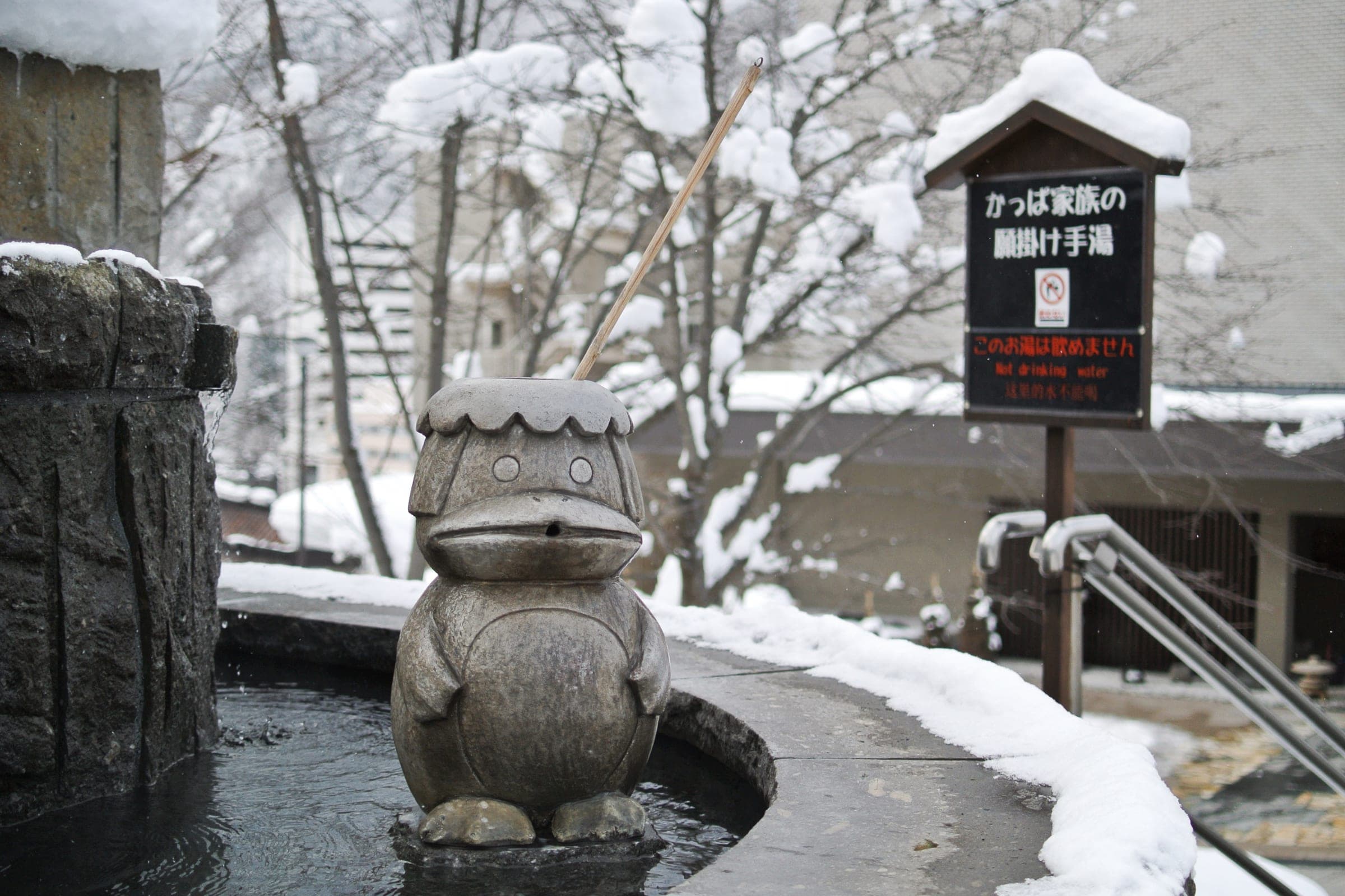 A stone kappa statue sits under fresh snow at a Jozankei Onsen foot bath