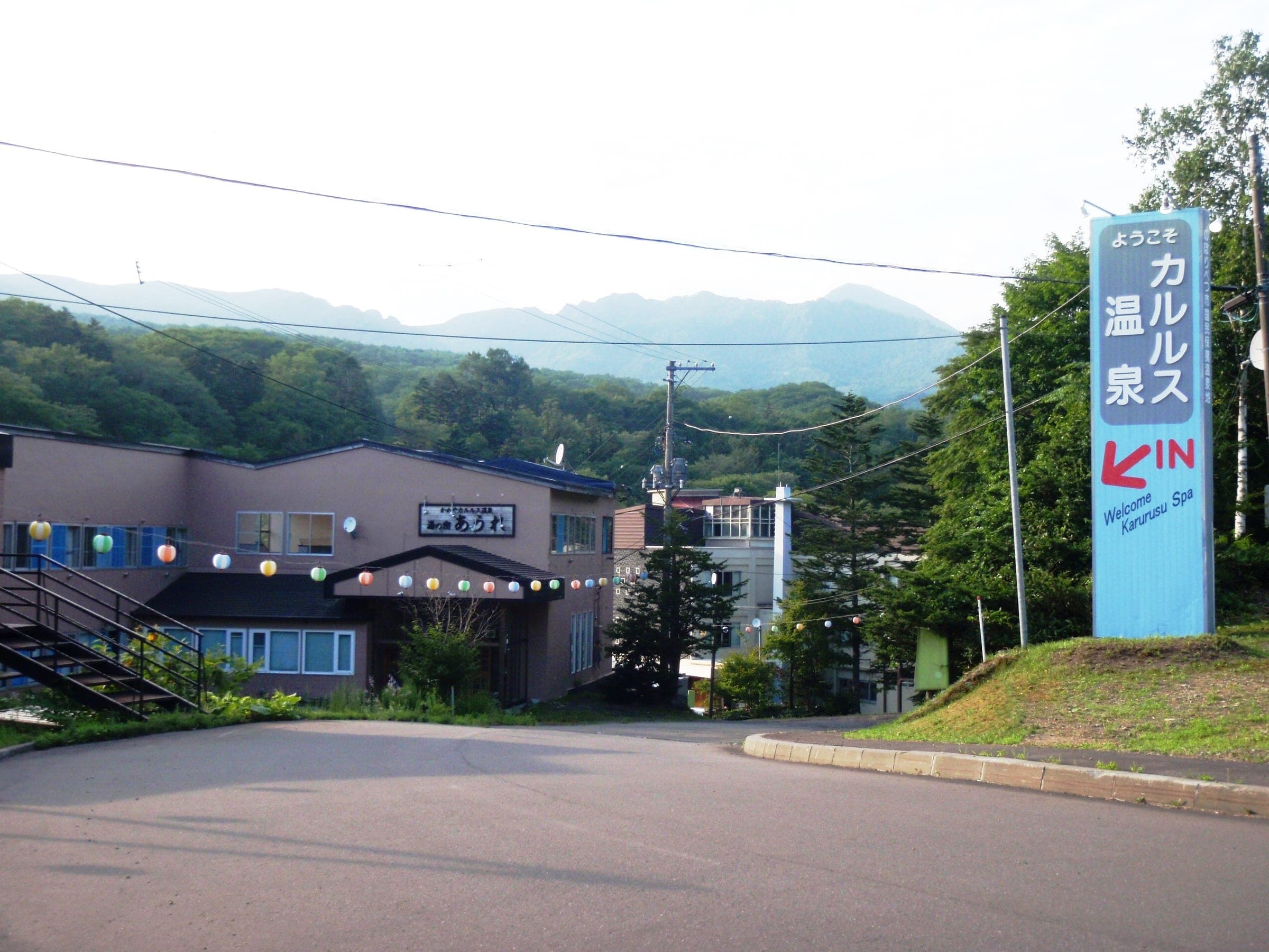 The entrance to Karurusu Onsen village with an inn, the village sign and green hills behind