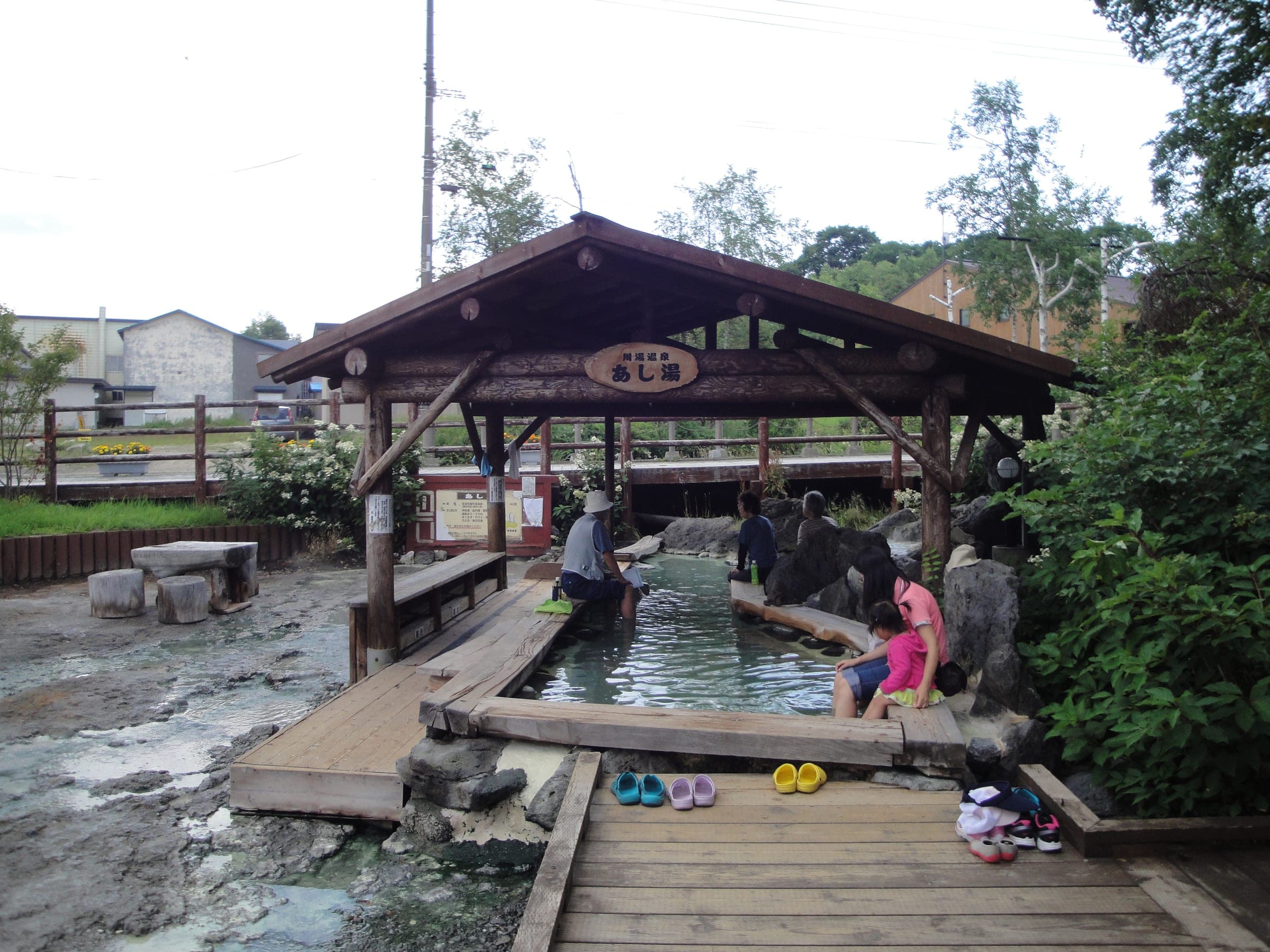 Bathers soak their feet under the wooden shelter of the Kawayu Onsen foot bath in summer