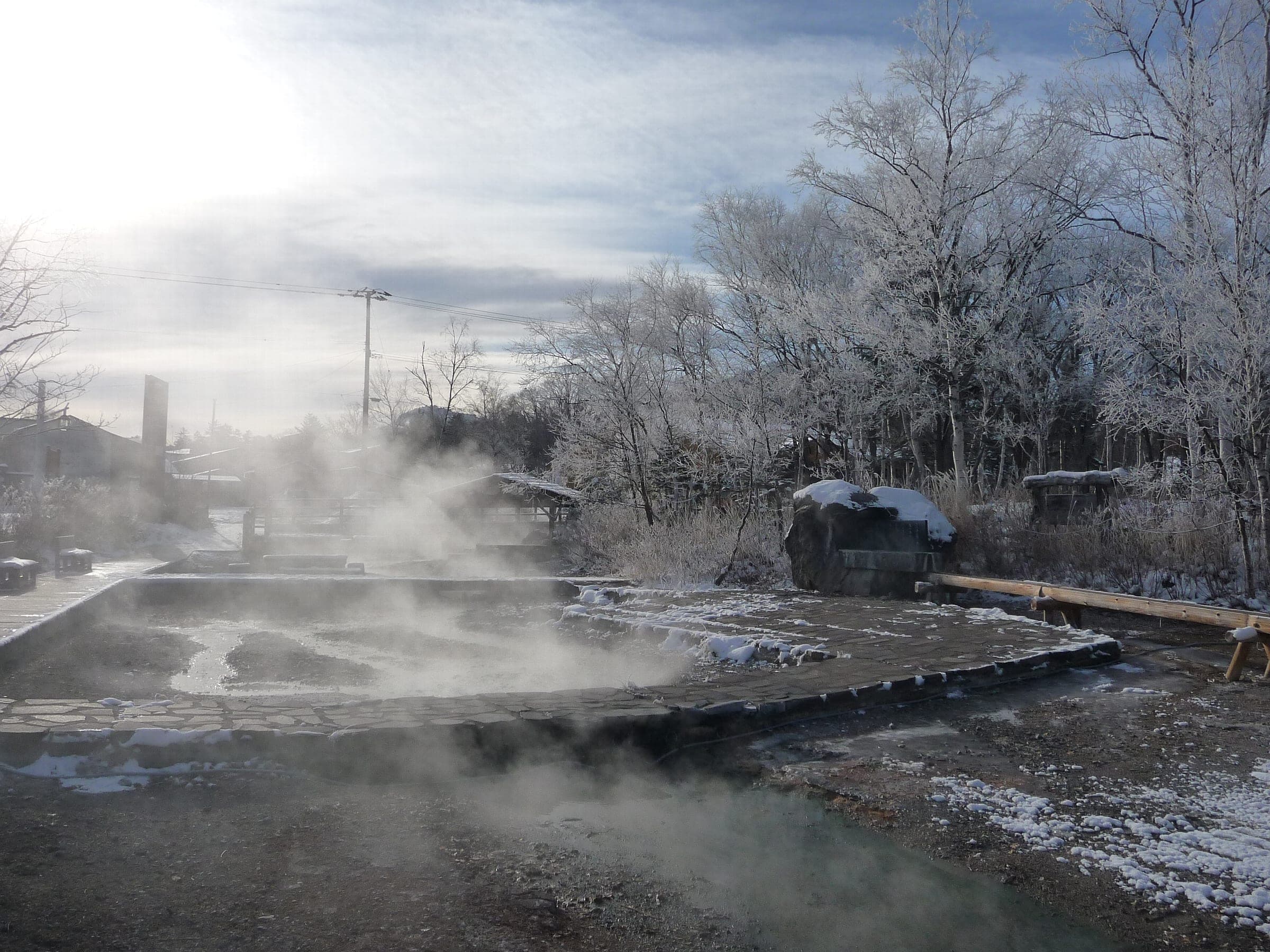 Steam drifts off the hot river through frosted trees in Kawayu Onsen