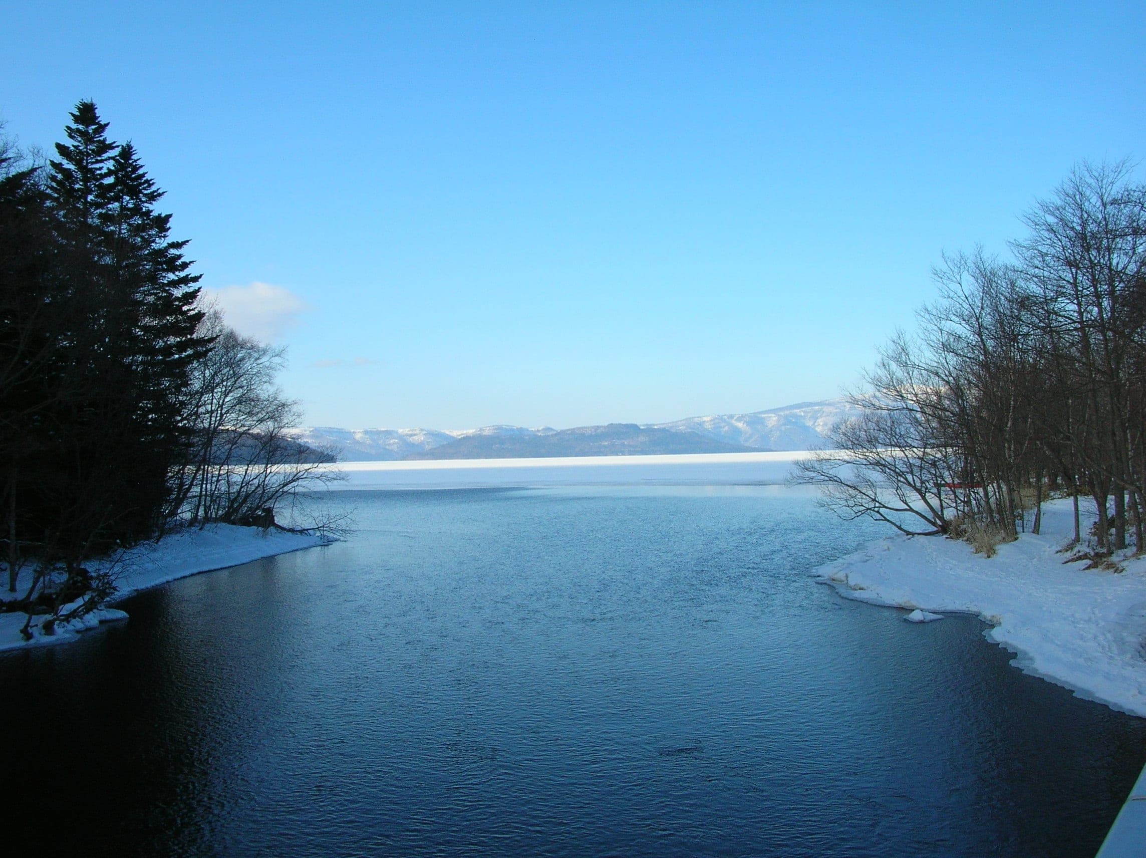 The Kushiro River leaves Lake Kussharo at Kotan between snowy banks under a blue sky