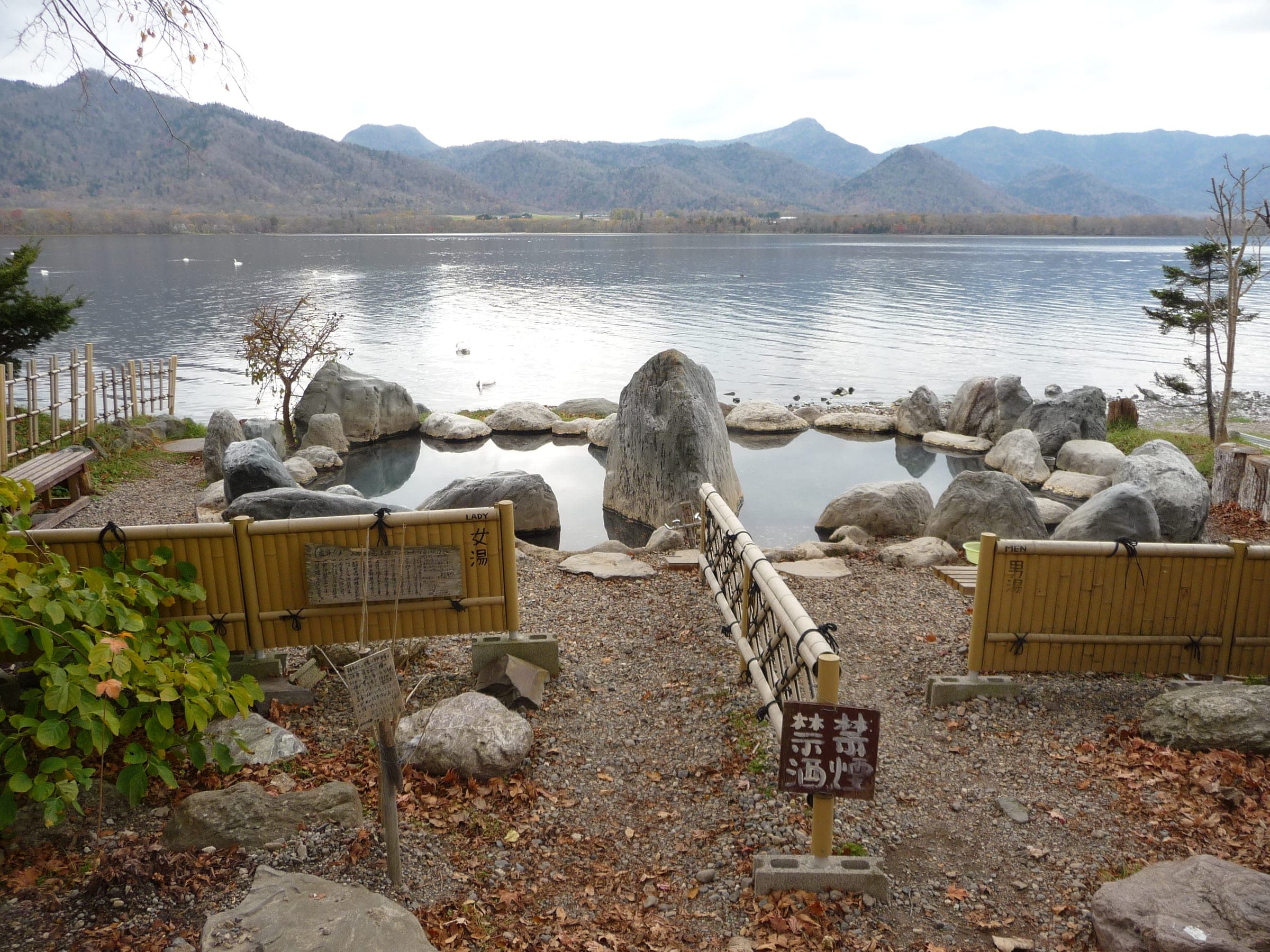 Kotan-no-yu's rock pool on the shore of Lake Kussharo with the caldera rim across the water
