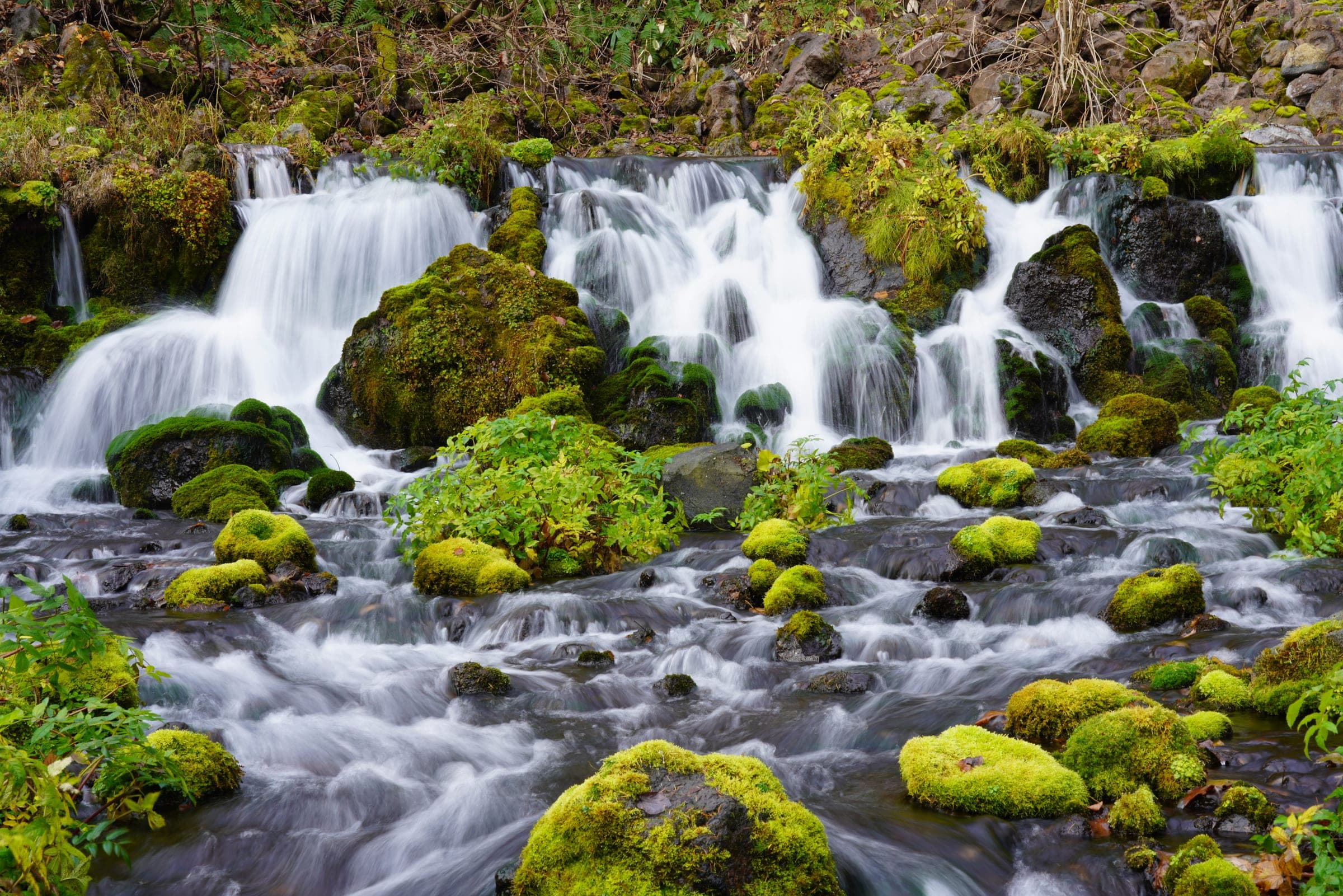 Spring water pours over mossy rocks at Fukidashi Park beside Kyogoku Onsen