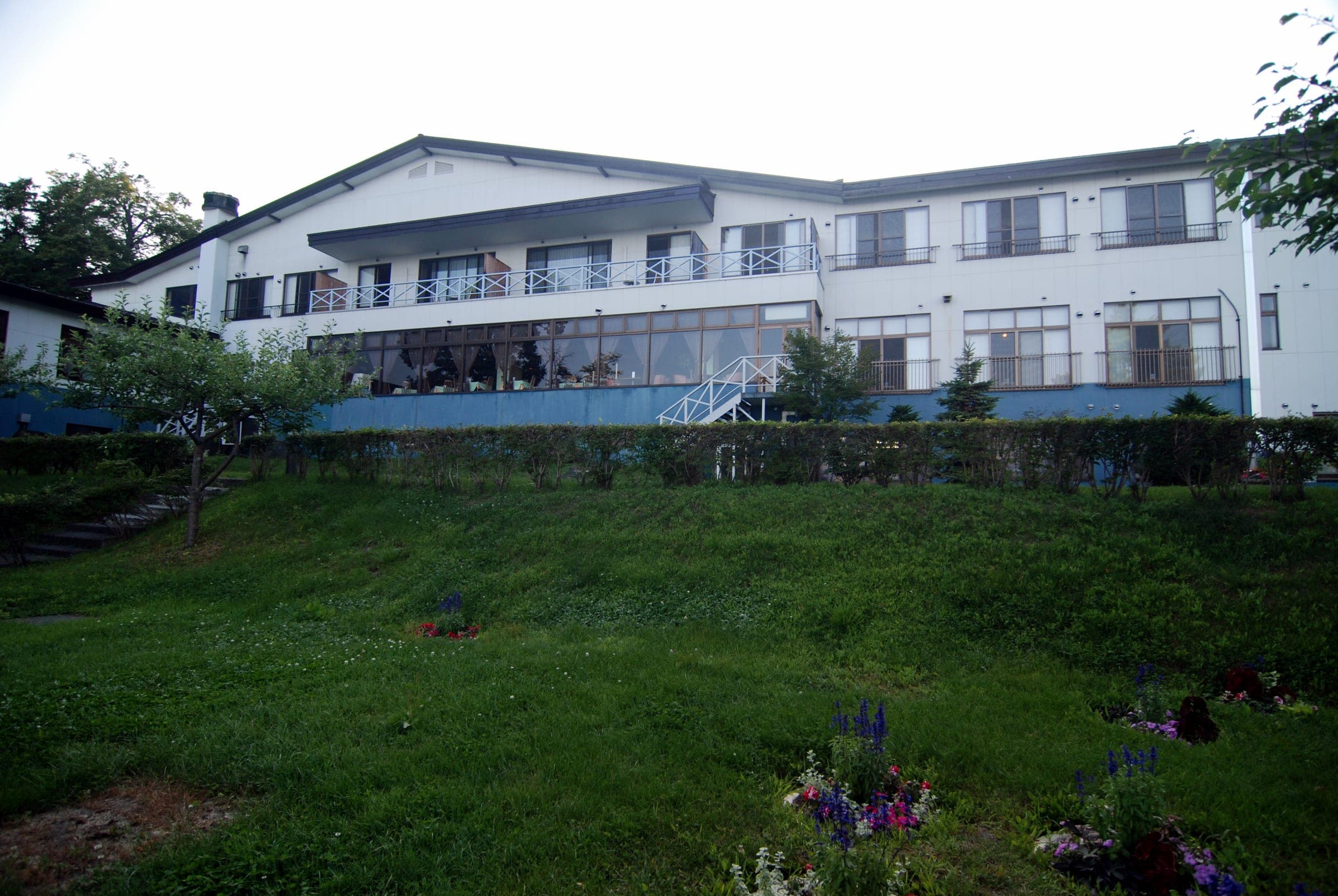 The white lakeside building of Marukoma Onsen Ryokan above a green lawn in summer