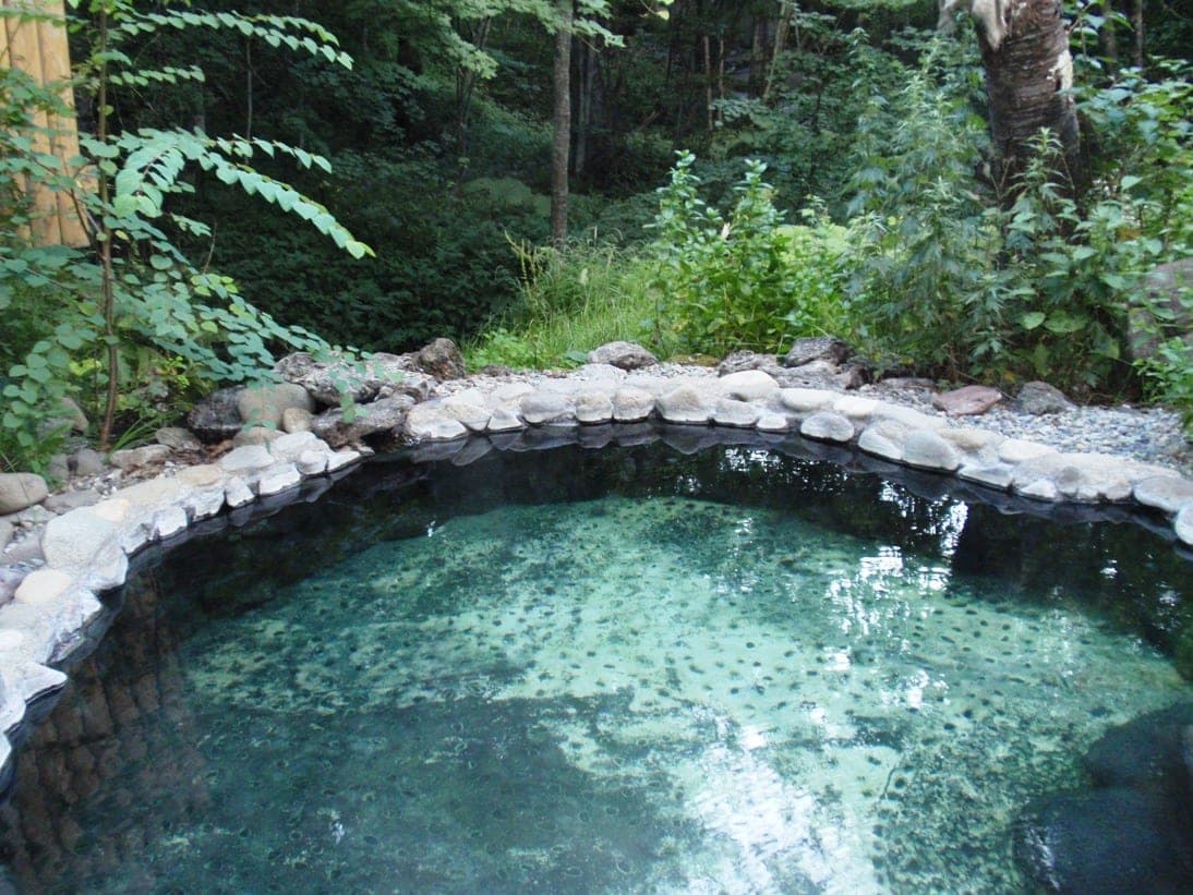 A round stone-edged rotenburo of clear water at Yumotokan in Nukabira