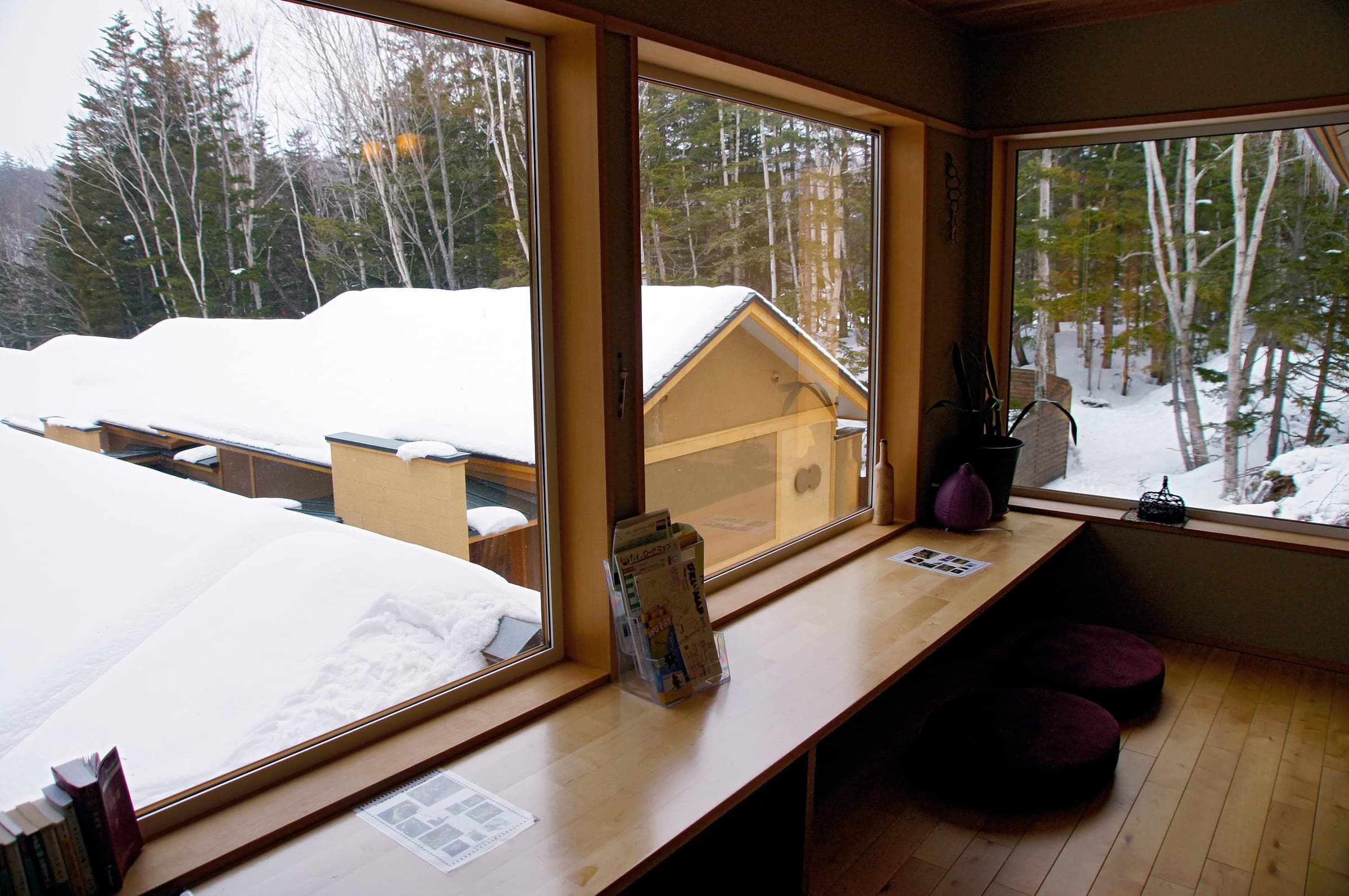 Snowy rooftops and birch trees seen through a lounge window at Mori-no-ryotei Biei