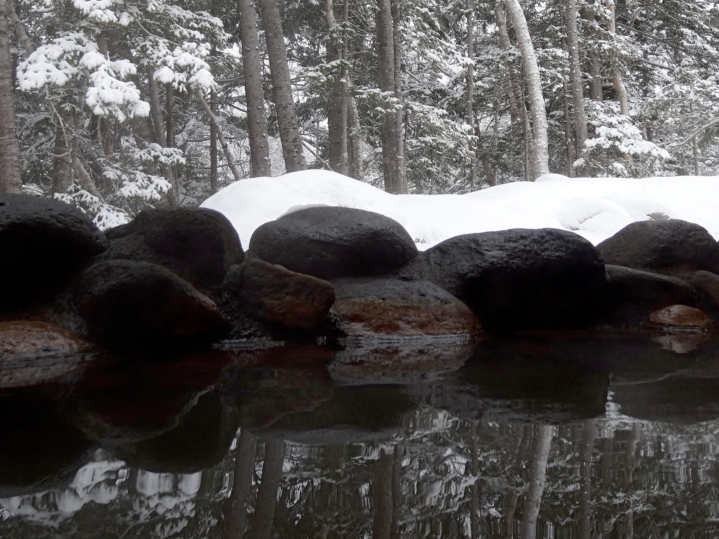 Snow caps the dark boulders around the outdoor bath at a Shirogane Onsen ryokan