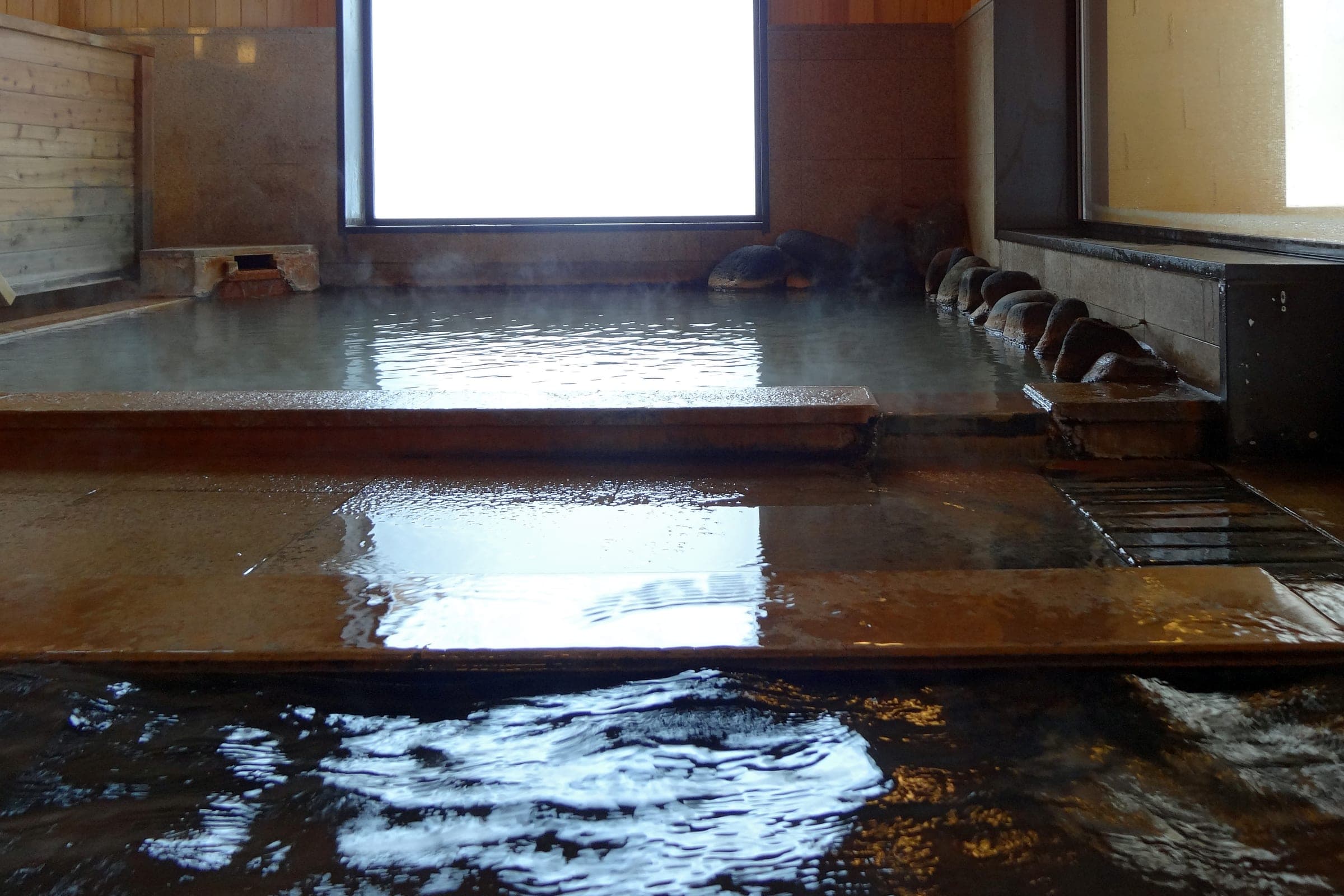 Spring water fills a long timber-edged indoor bath at Mori-no-ryotei Biei in Shirogane Onsen