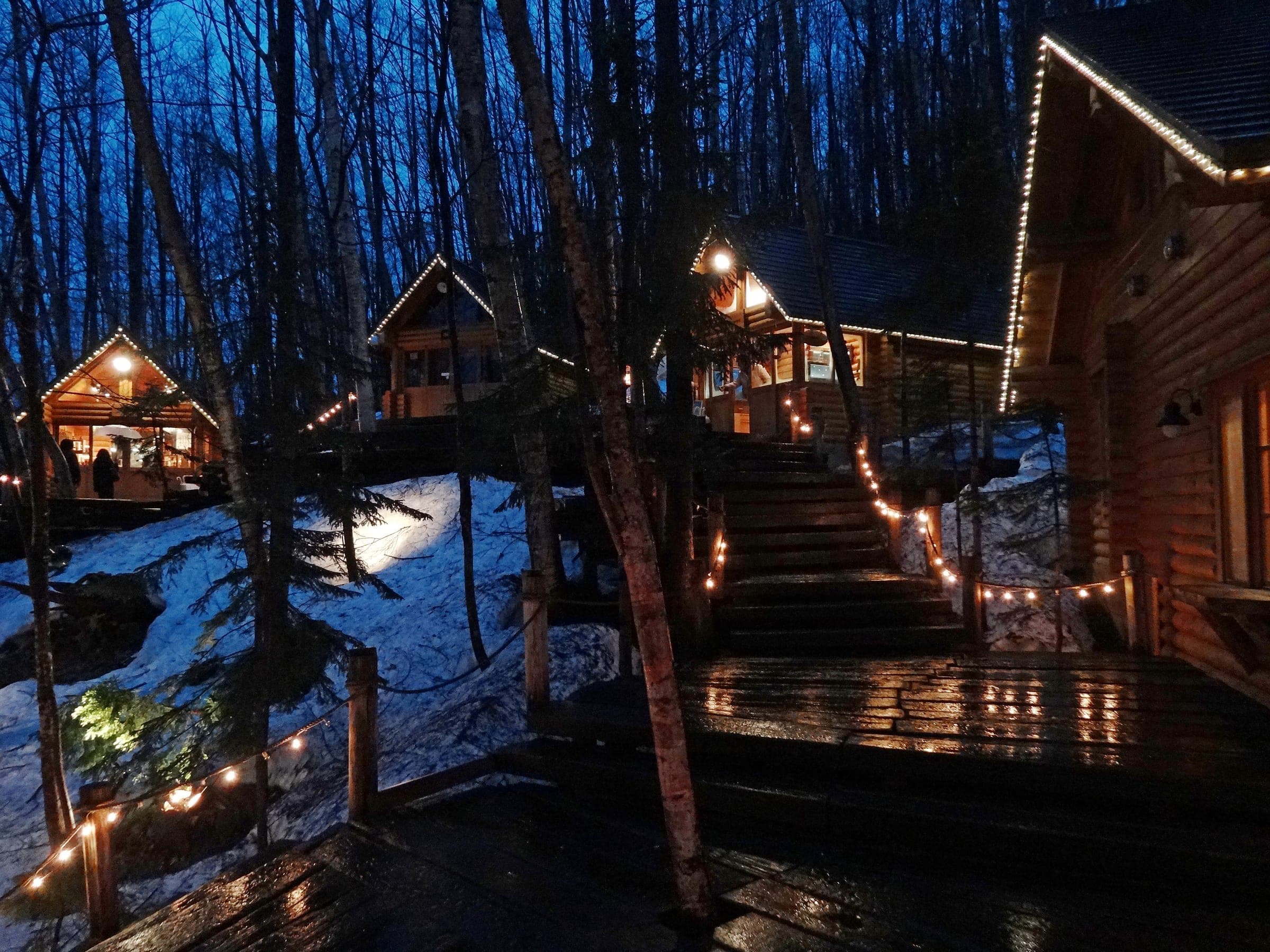 Lit log cabins of Ningle Terrace in the forest beside the New Furano Prince Hotel at dusk