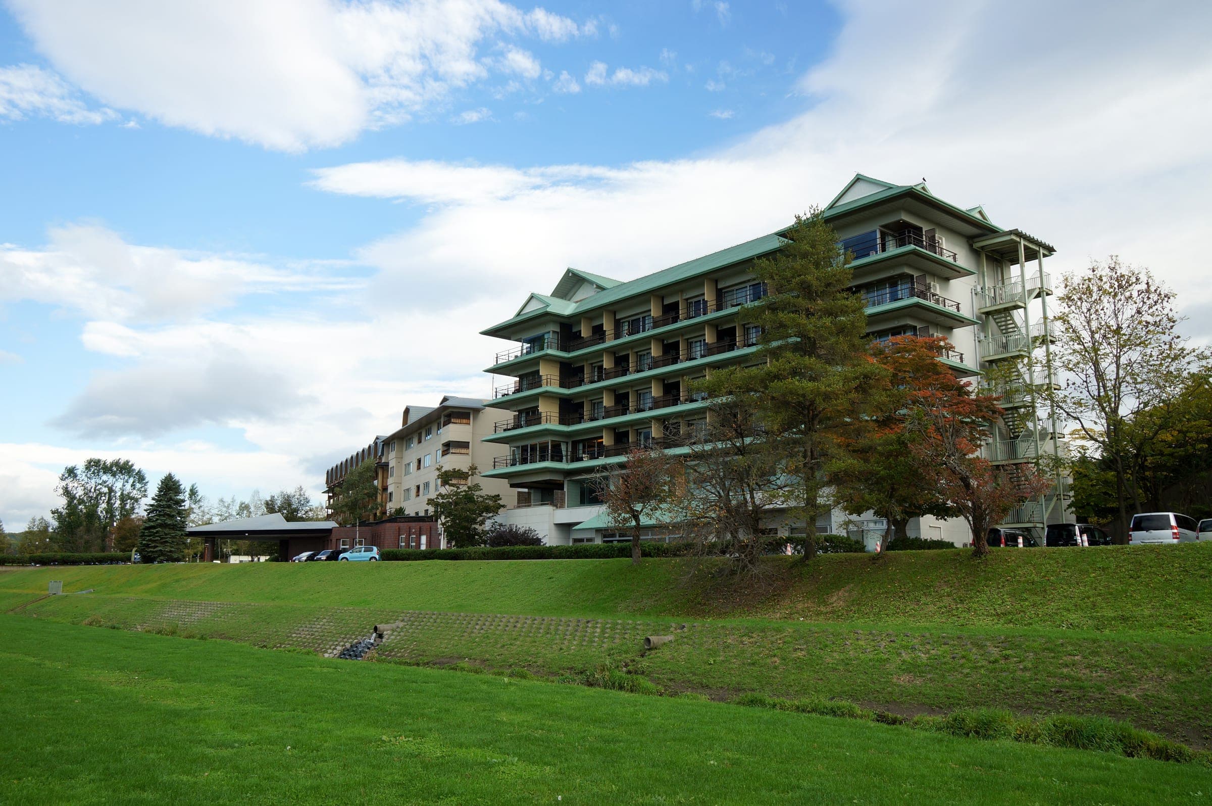 A tiered hotel stands above a green lawn at Tokachigawa Onsen under a blue sky