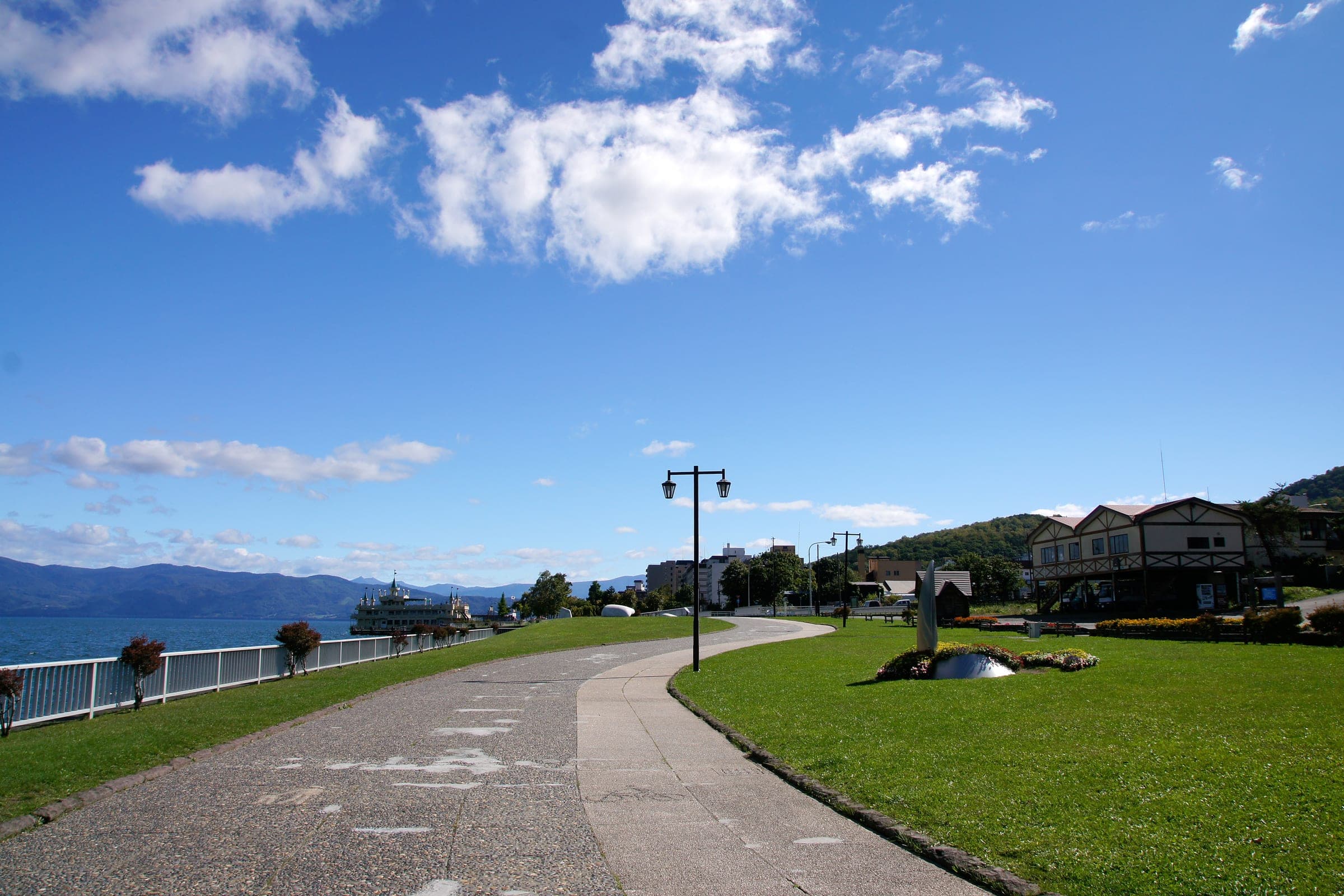 The lakeside promenade at Toyako Onsen runs past hotels under a blue sky
