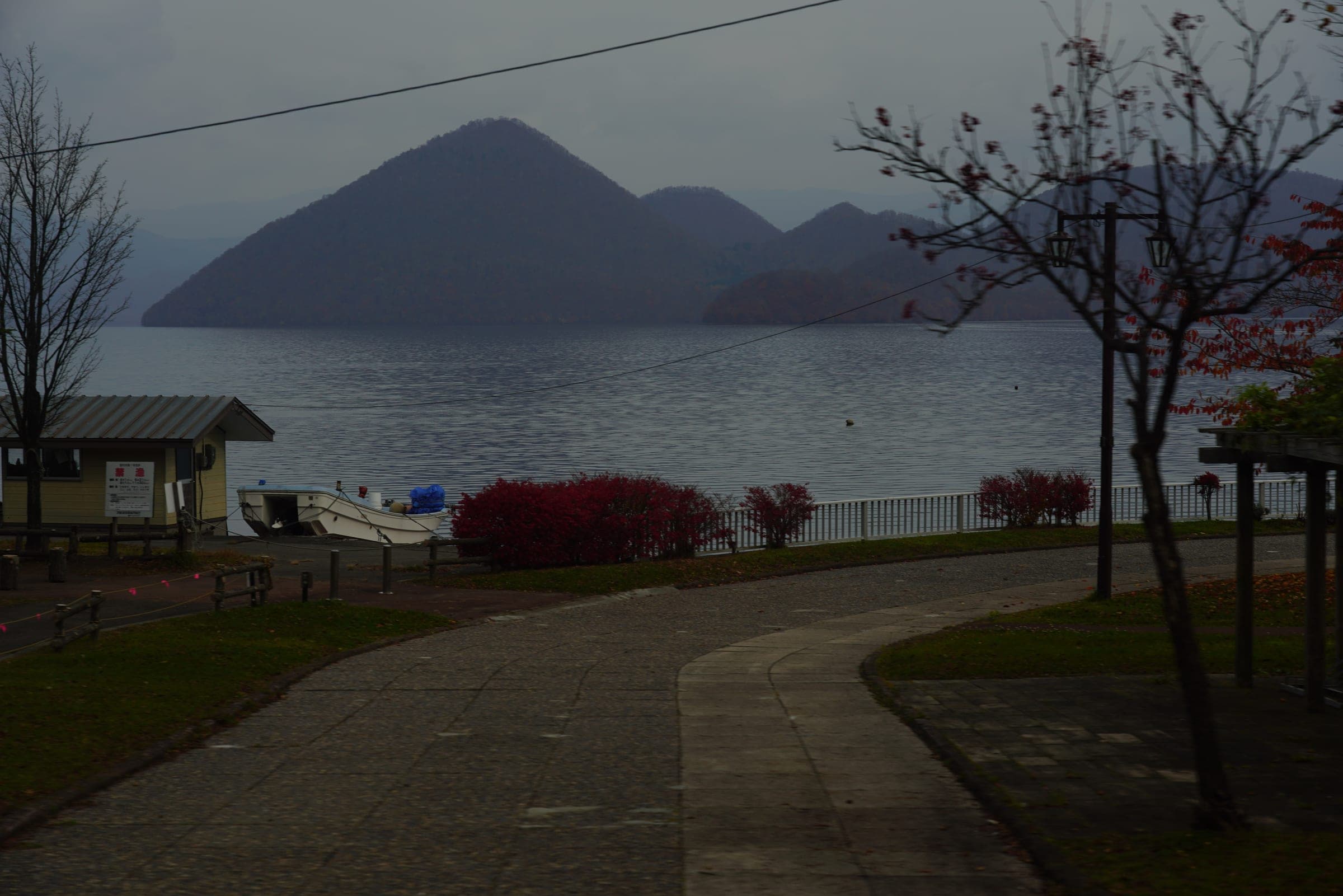Autumn shrubs on the Toyako Onsen shore look across grey water to Nakajima