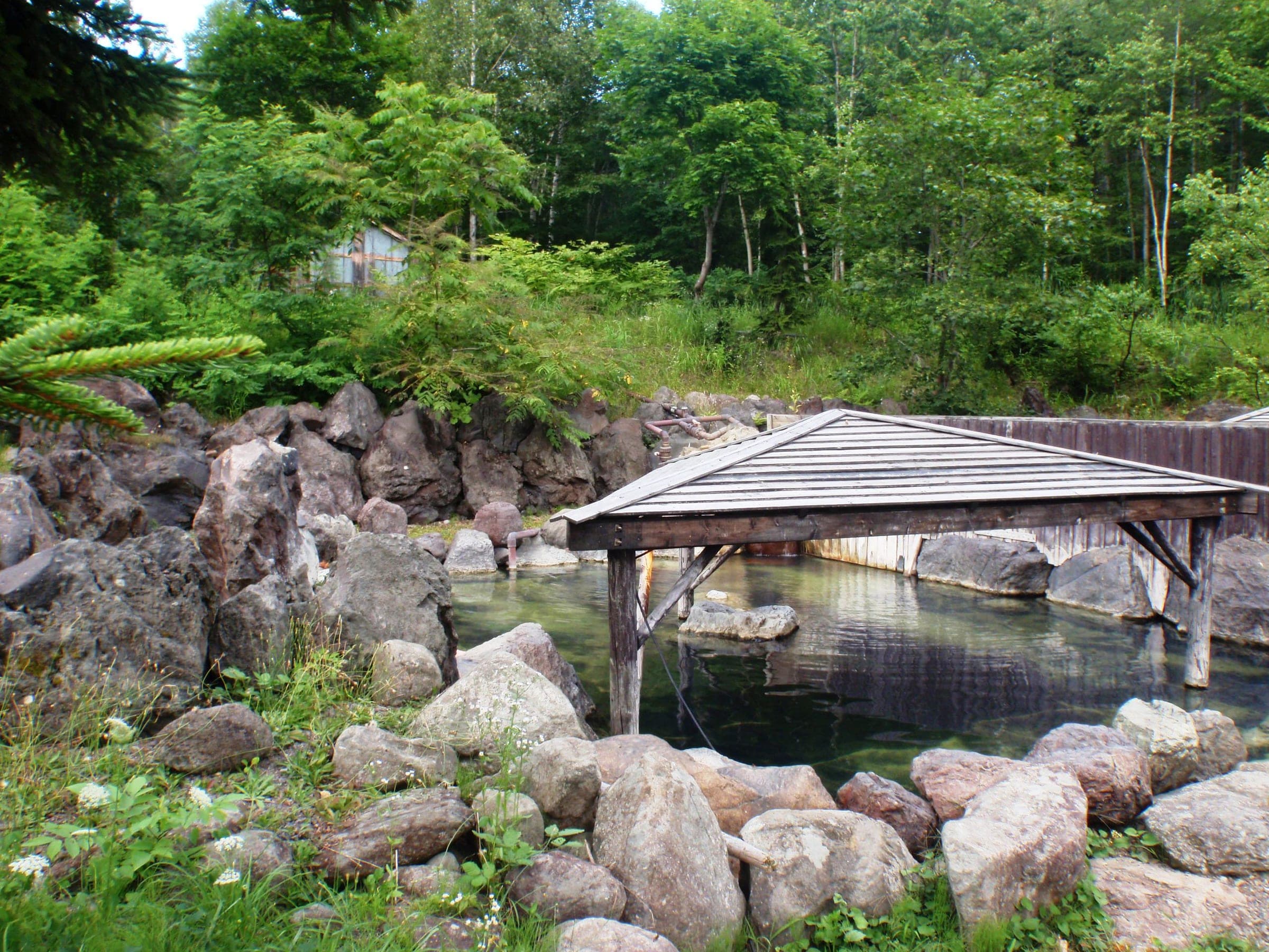 A wooden roof shelters the rock-lined outdoor bath at Yugokorotei, surrounded by forest