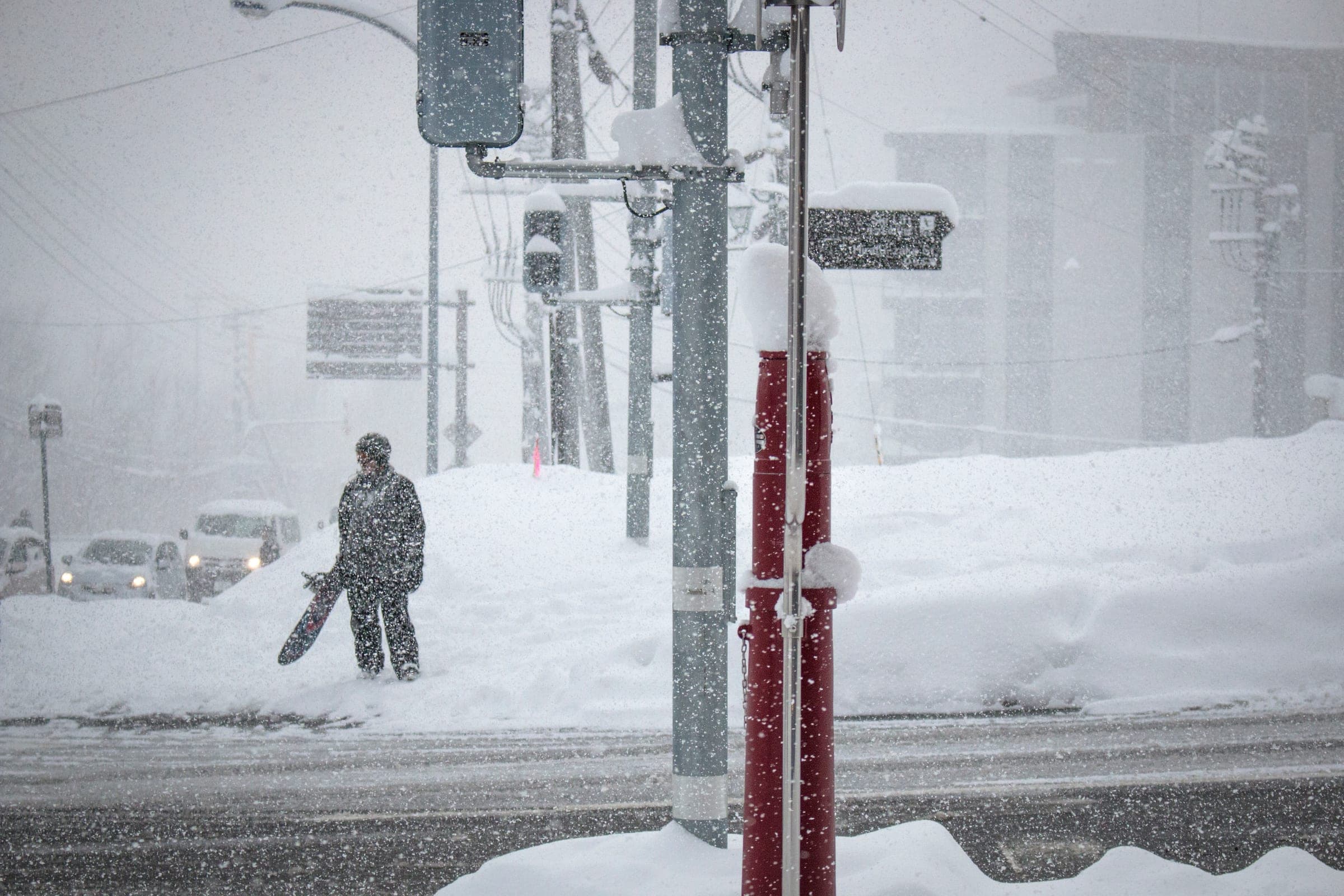 A snowboarder waits out heavy snowfall at a lower Hirafu crossing, a short walk from Yukoro Onsen