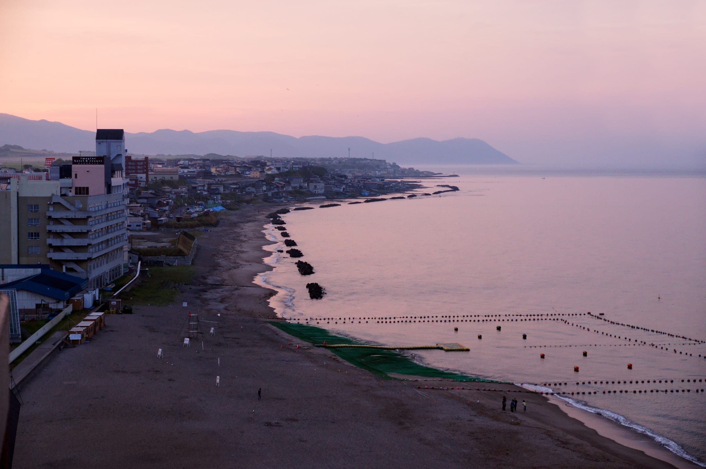 Hotels of Yunokawa Onsen face a quiet beach under a pink dusk sky