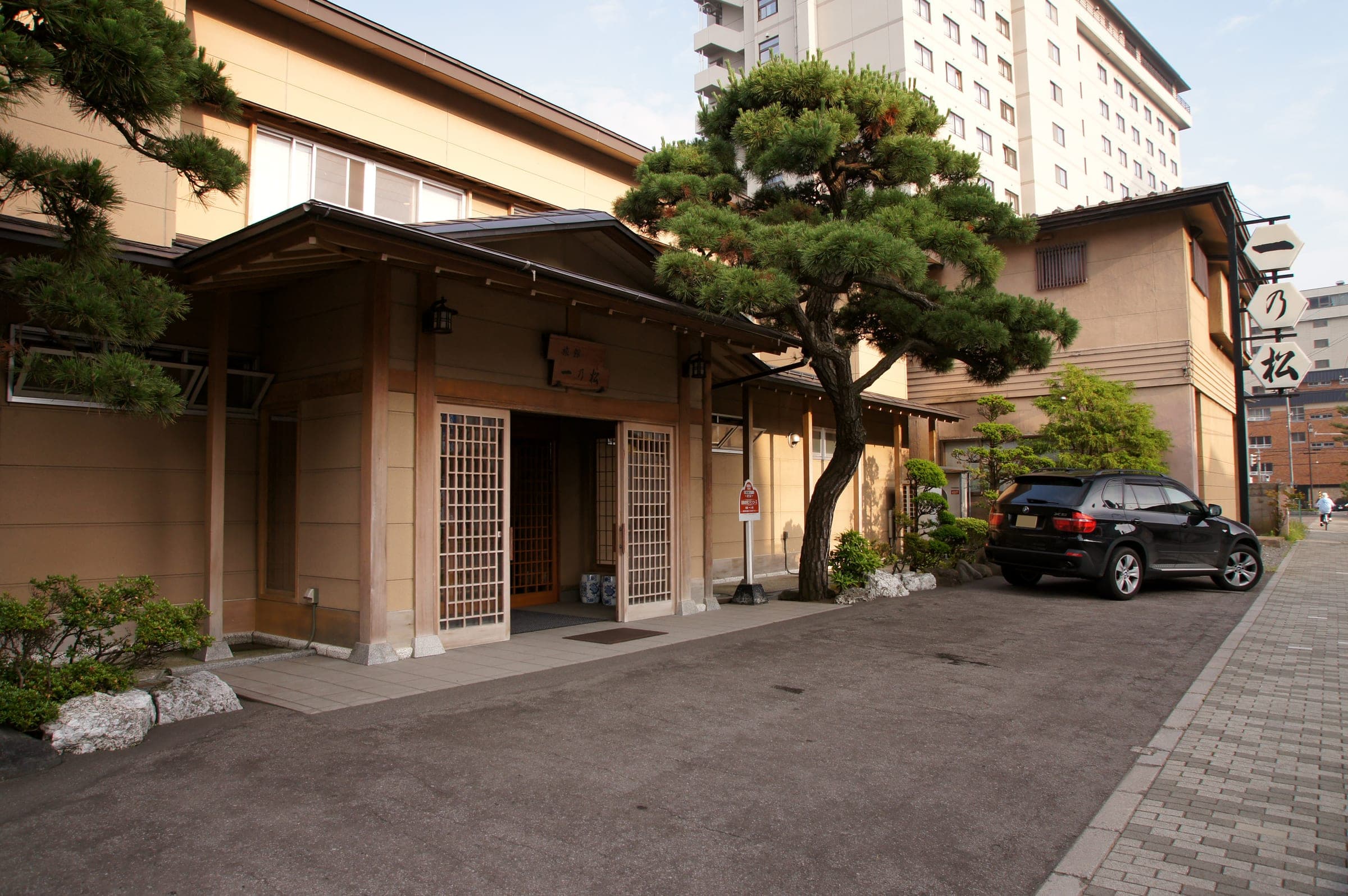 A traditional ryokan entrance with a pruned pine on a street in Yunokawa Onsen
