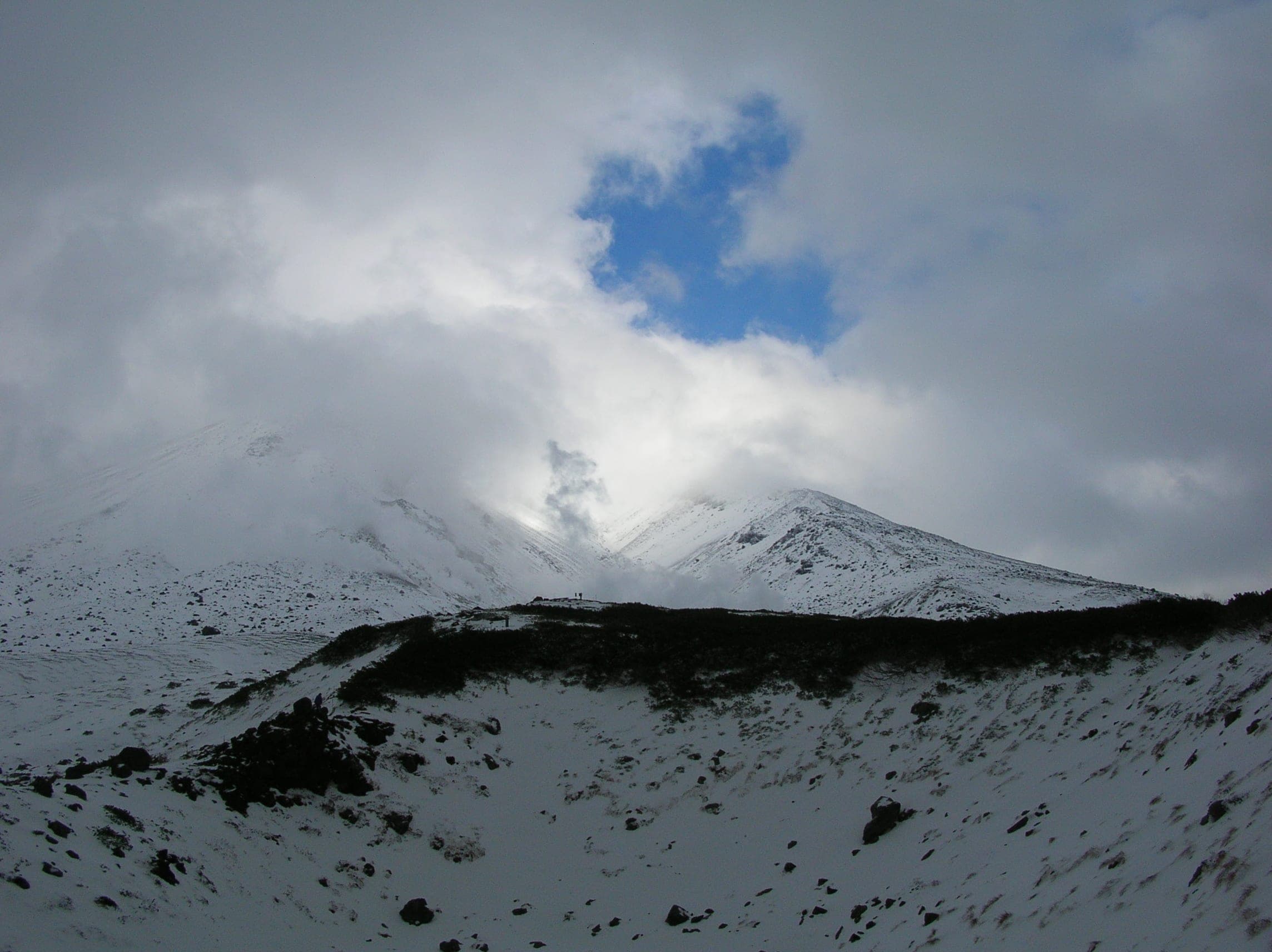 Clouds part over Asahidake's snow-covered summit in early winter, with dark creeping pine below