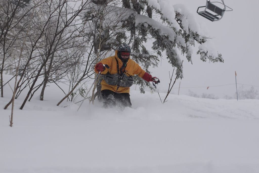 A skier in a yellow jacket ploughs through deep powder below a chairlift at Furano