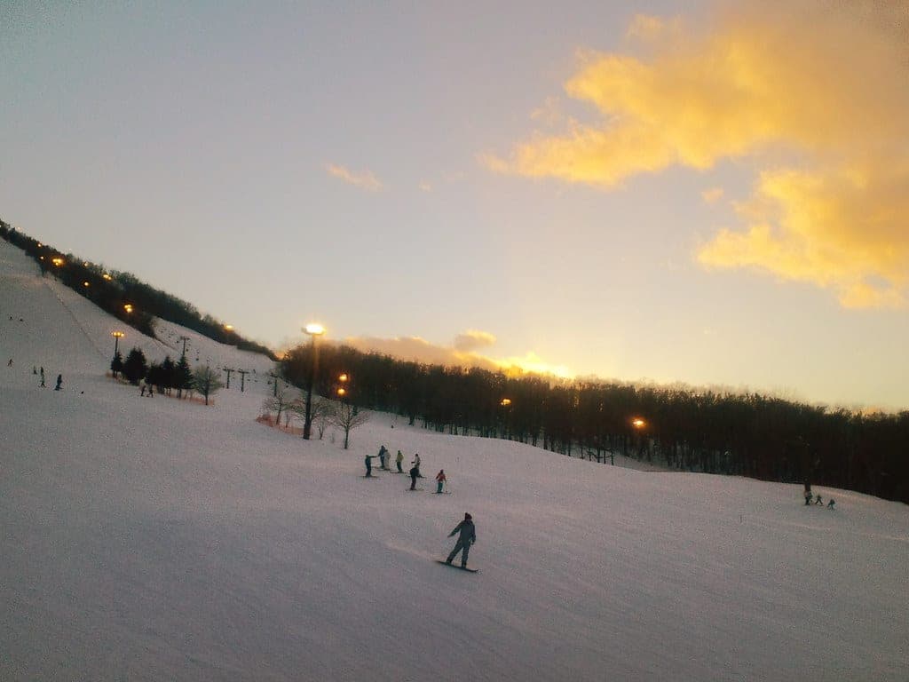 Skiers trace the lower slope at Fu's Snow Area as the sun sets behind the trees