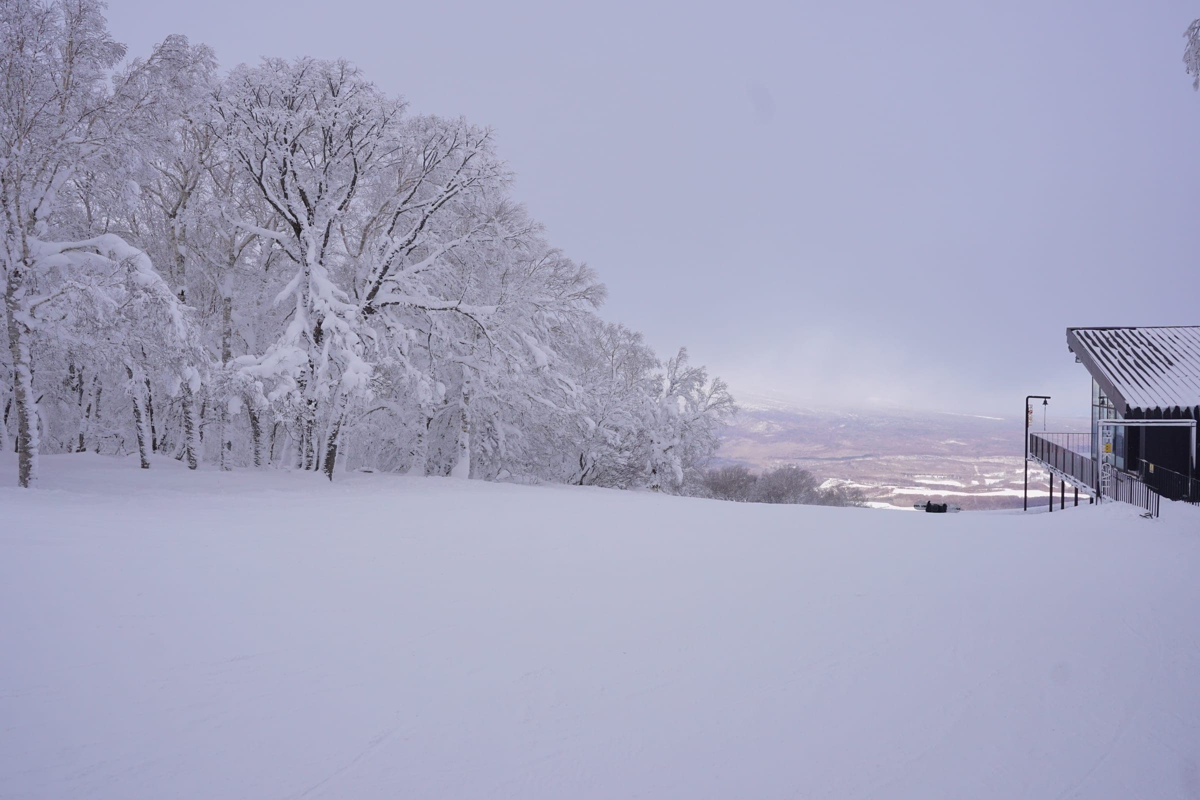 A wide snowy slope beside the top station at Hakodate Nanae Snowpark looks out over the plain