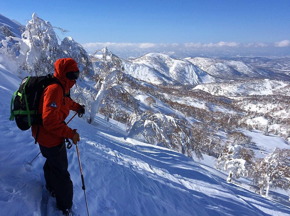 A skier in a red jacket looks over rime-coated ridges in the sidecountry at Kiroro