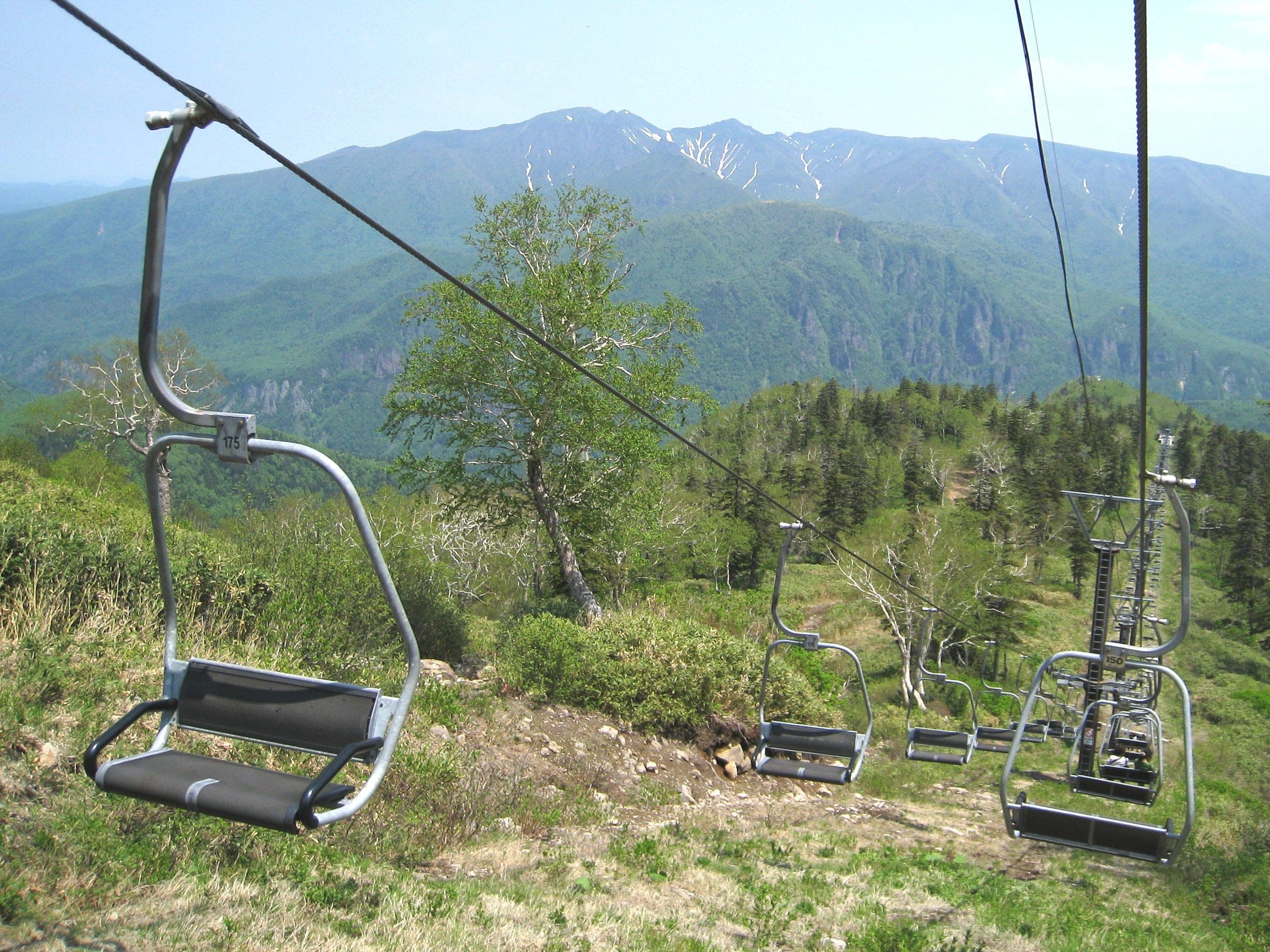 The Kurodake chairlift climbs through summer scrub with the Daisetsuzan peaks behind
