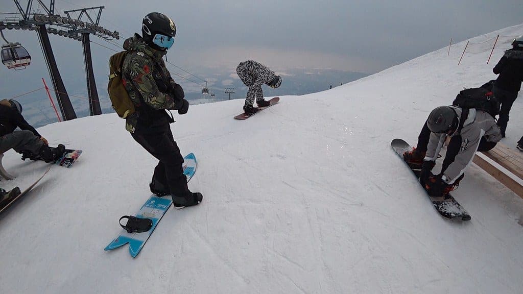 Snowboarders strap in at the top of the Niseko Annupuri gondola before dropping in