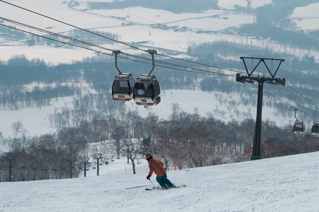 A skier carves down a groomed run under the Niseko Annupuri gondola above snowy farmland