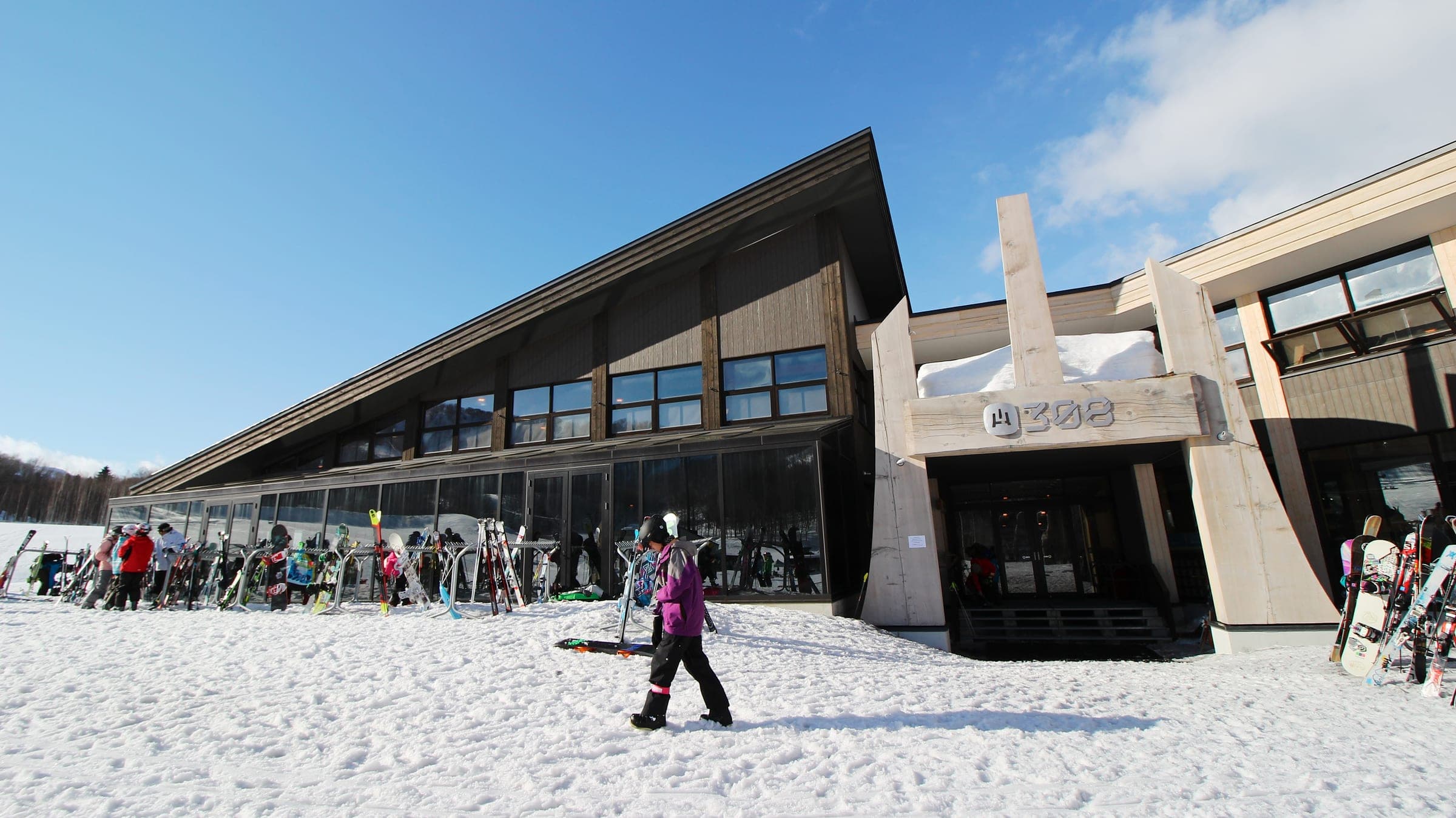 Skiers gather on the snow outside the angular HANAZONO 308 base building at Niseko HANAZONO